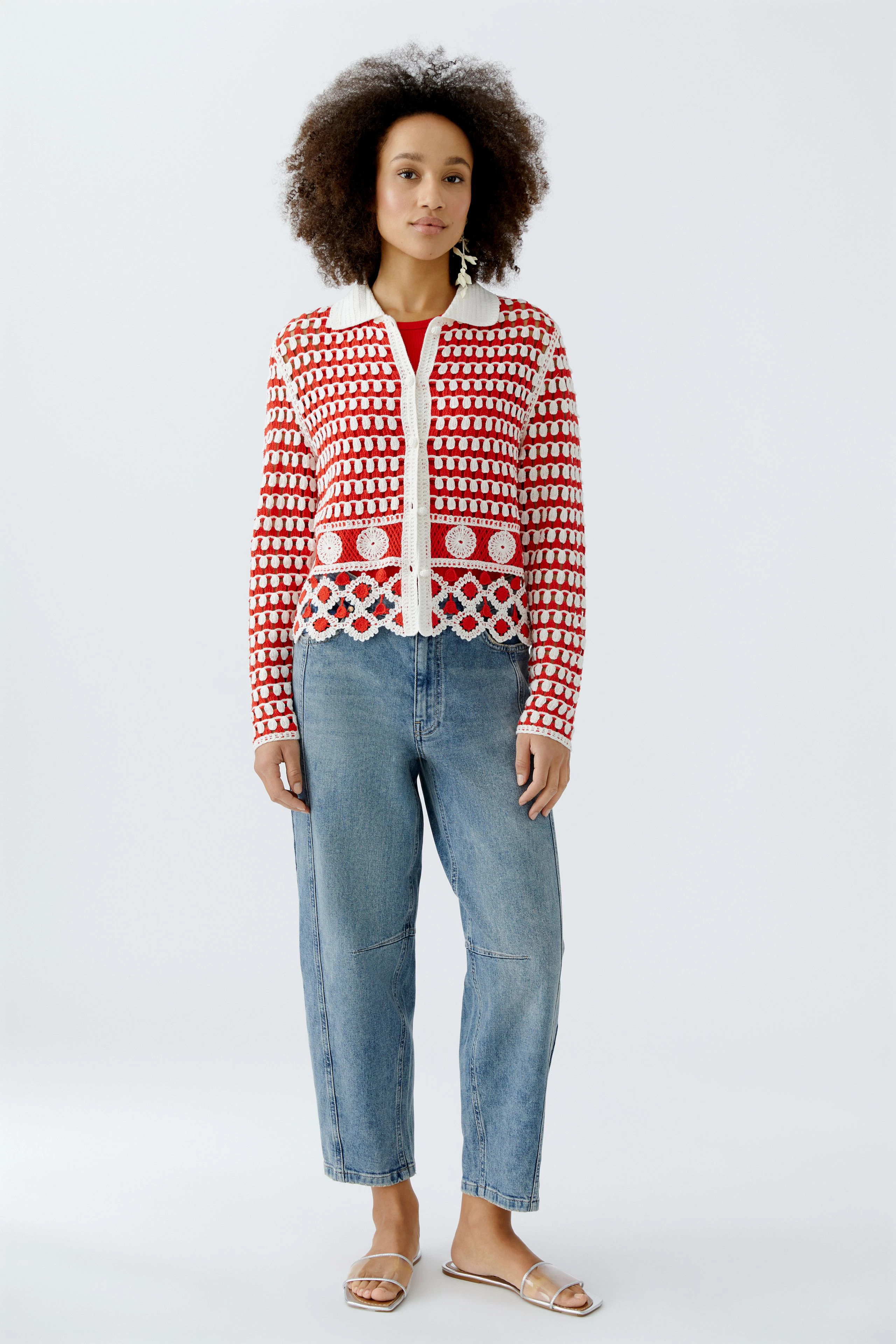 Bunte Damen-Strickjacke mit geometrischem Muster, lässig kombiniert mit Jeans und Sandalen.