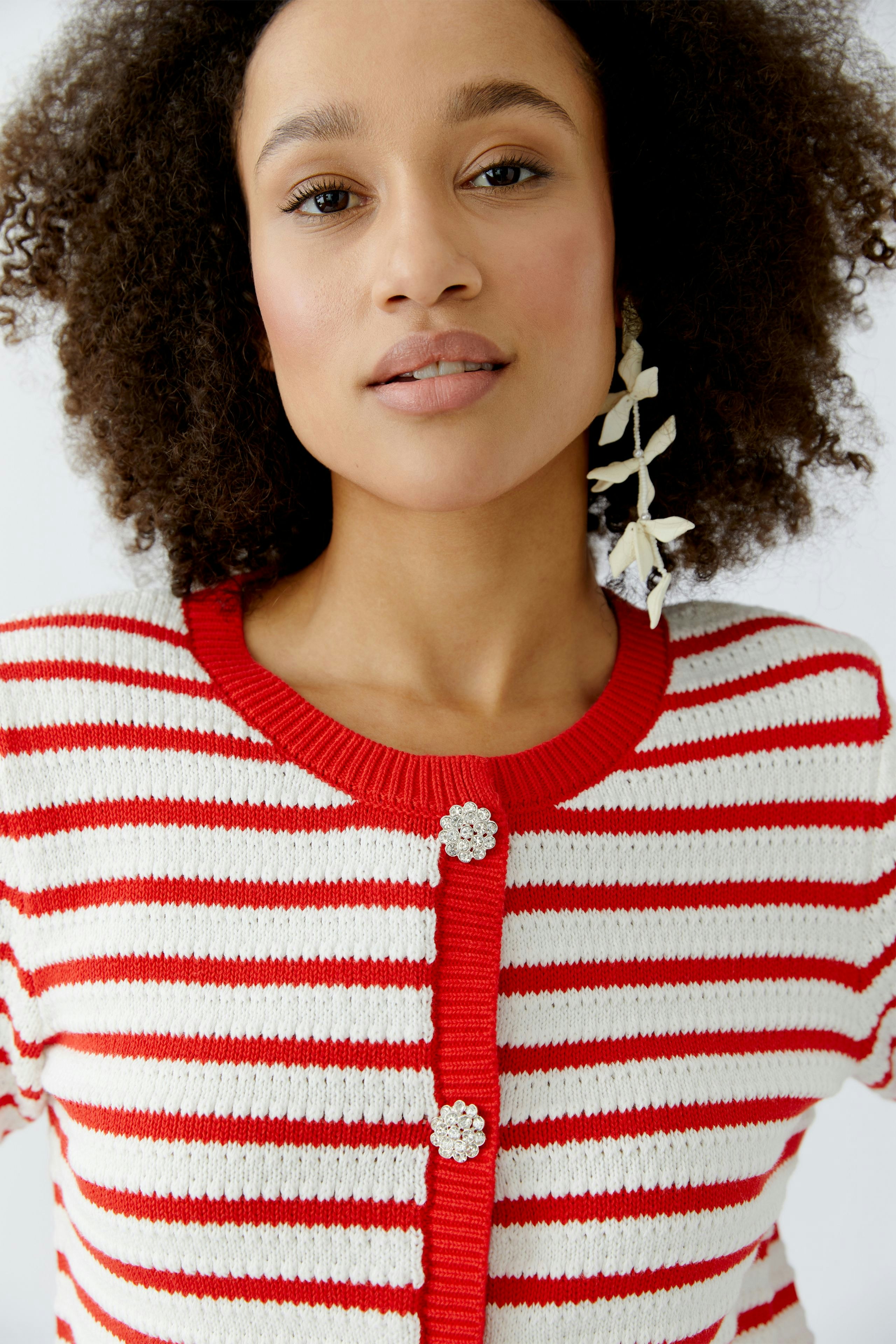 Damen-Strickjacke: Frau mit lockigen Haaren trägt eine rot-weiß gestreifte Strickjacke mit Knöpfen.