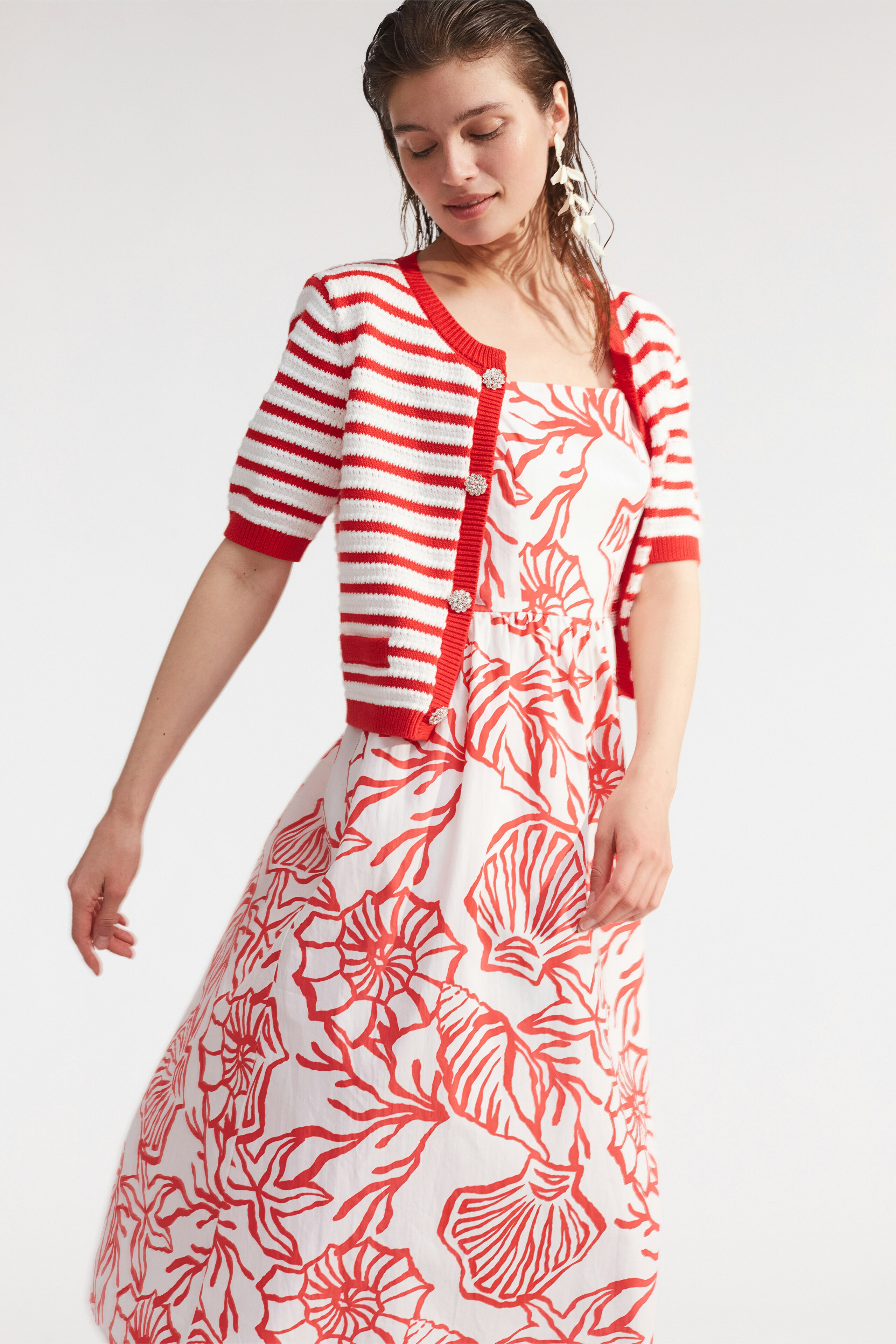 Damen-Strickjacke: Frau in gestreifter, roter Strickjacke über einem weißen Kleid mit floralen Mustern.