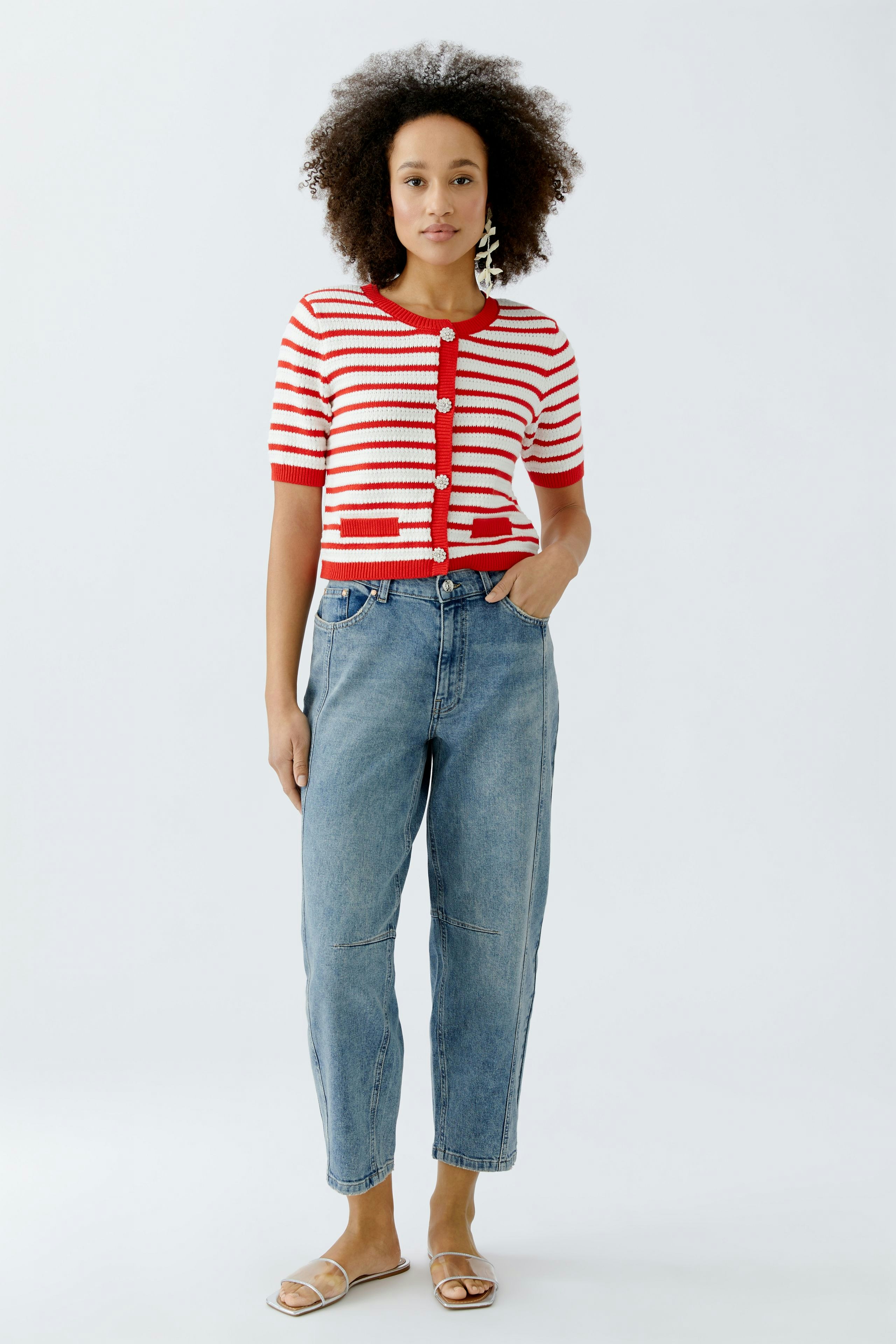 Damen-Strickjacke: Frau in gestreifter, roter und weißer Strickjacke mit kurzen Ärmeln und lässigen Jeans.