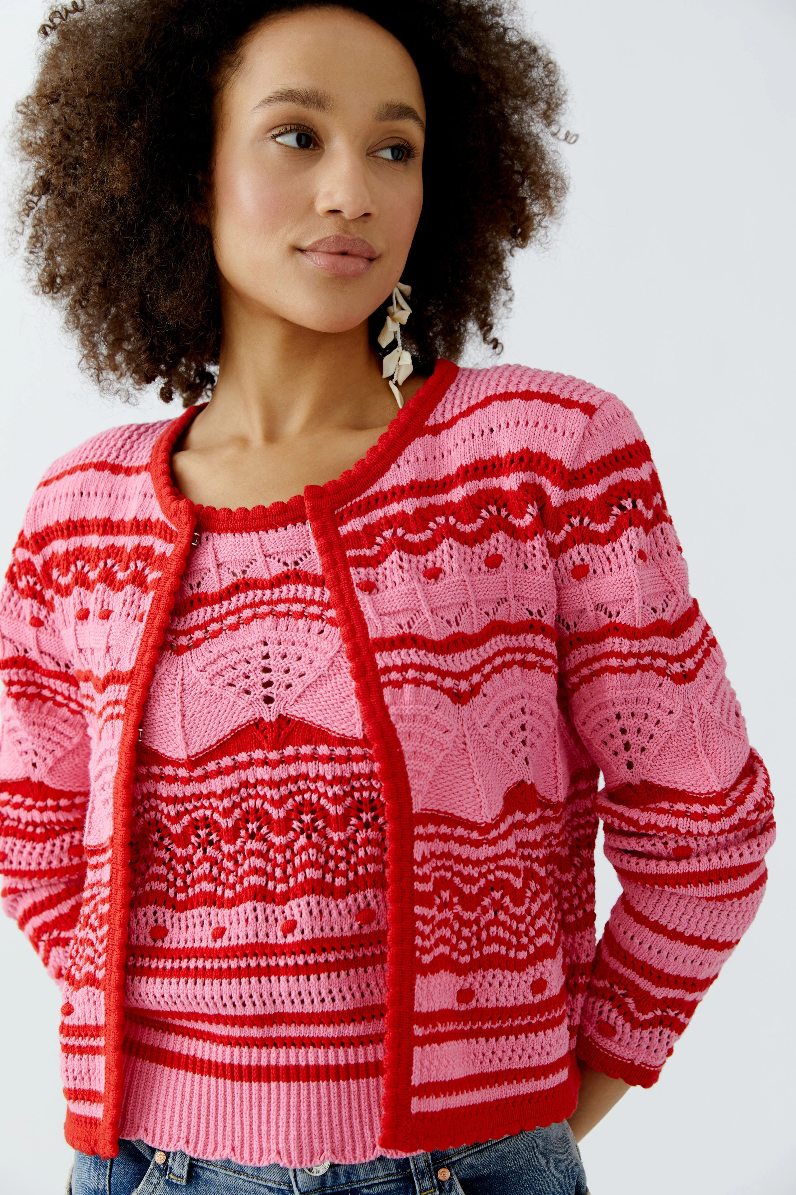 Bunte Damen-Strickjacke: Frau trägt eine pink-rote Strickjacke mit auffälligem Muster und lässigem Look.