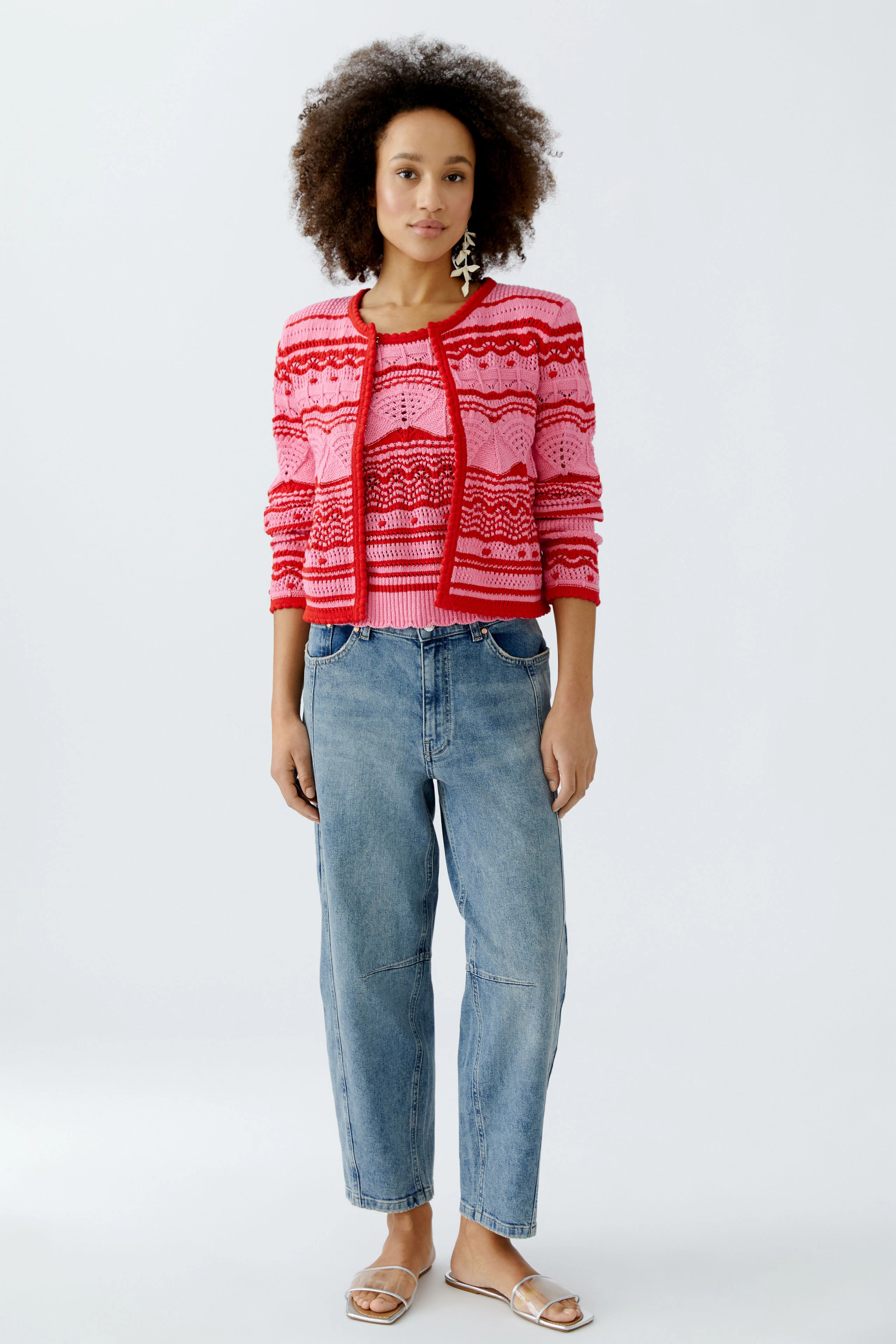 Bunte Damen-Strickjacke mit geometrischem Muster, kombiniert mit lässigen Jeans und Sandalen.