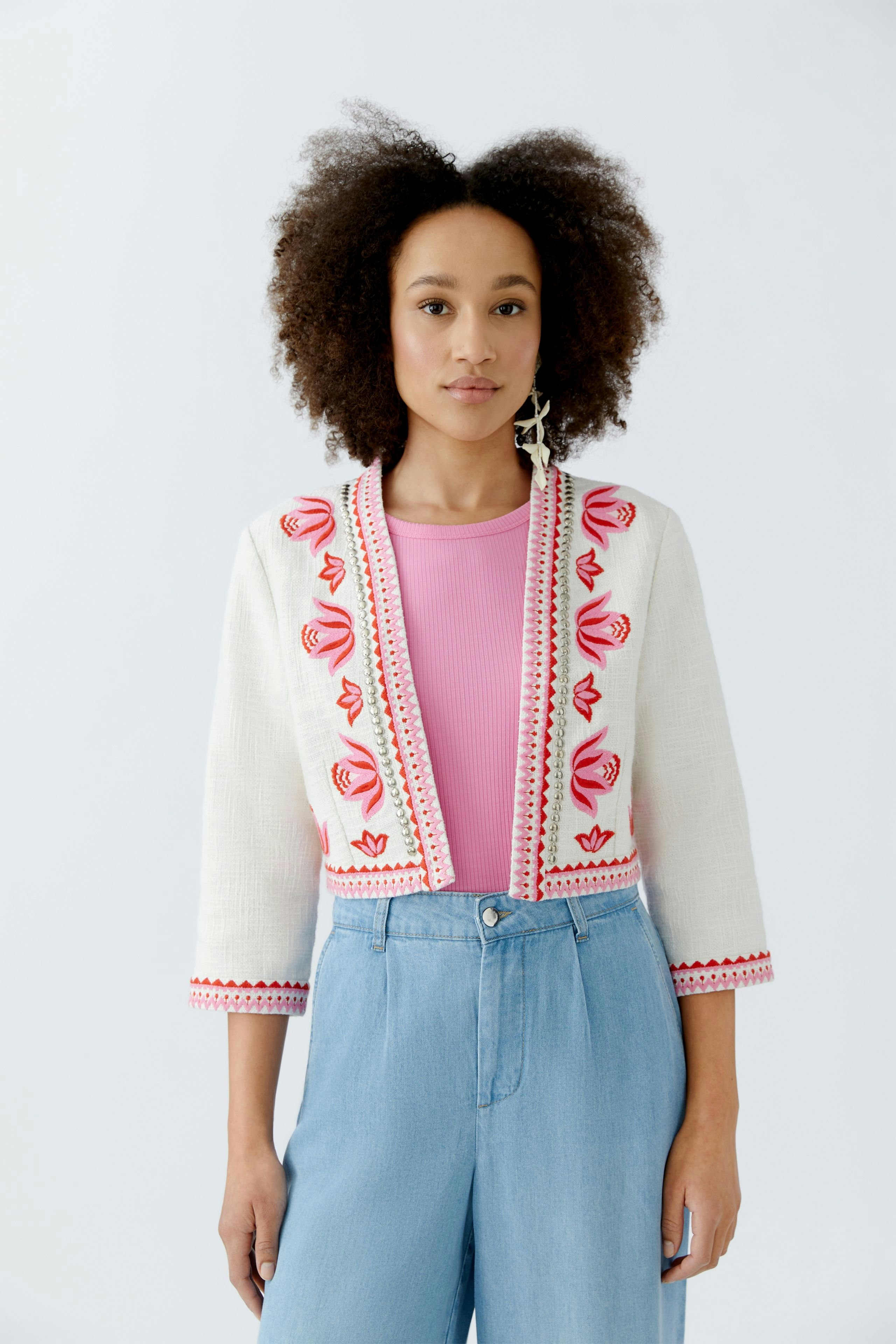 Stylish women's jacket: A woman in a white jacket with red embroidery over a pink top and blue jeans.