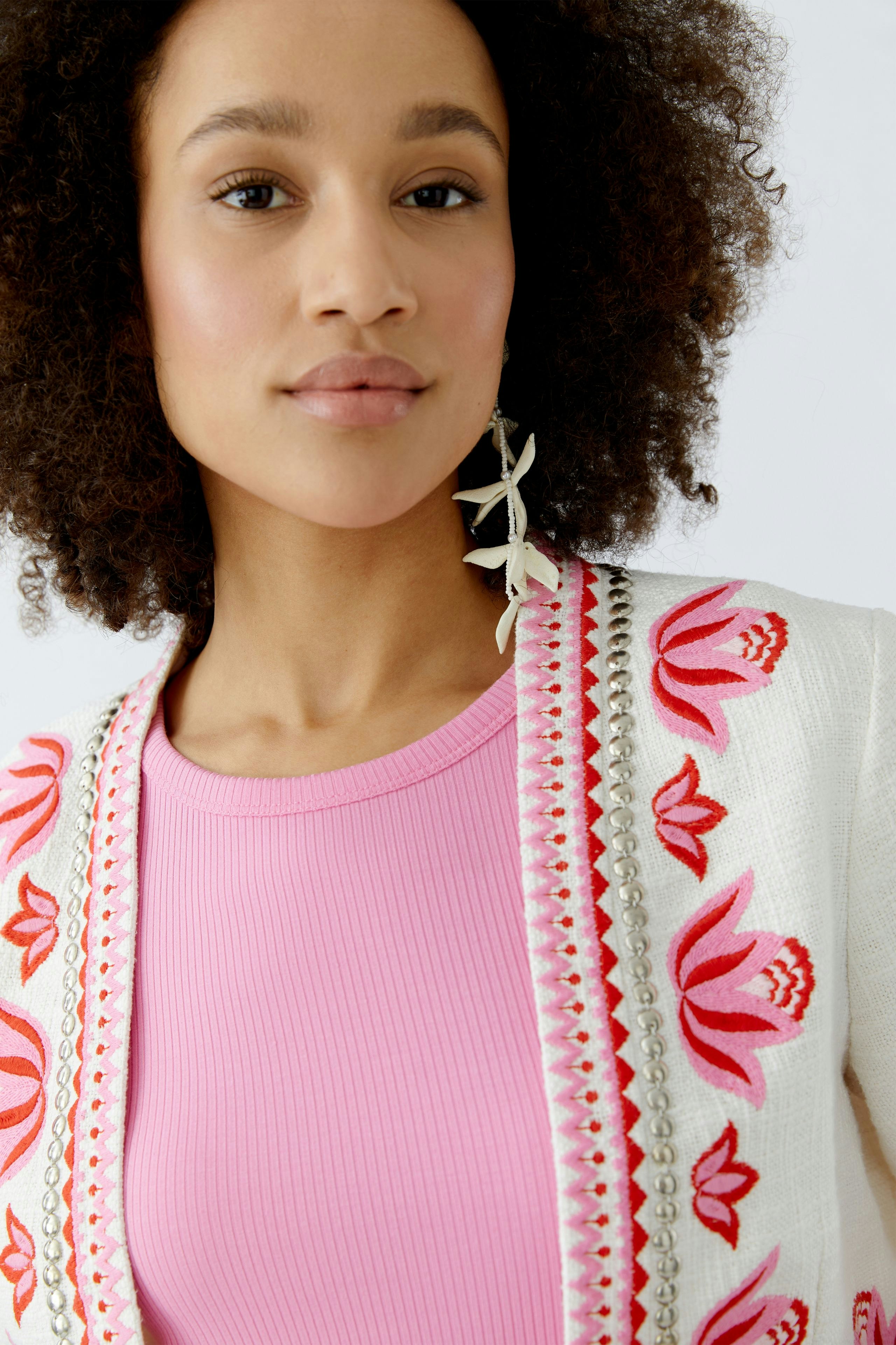 Stylish women's jacket: Close-up of a woman wearing a floral embroidered jacket over a pink top.