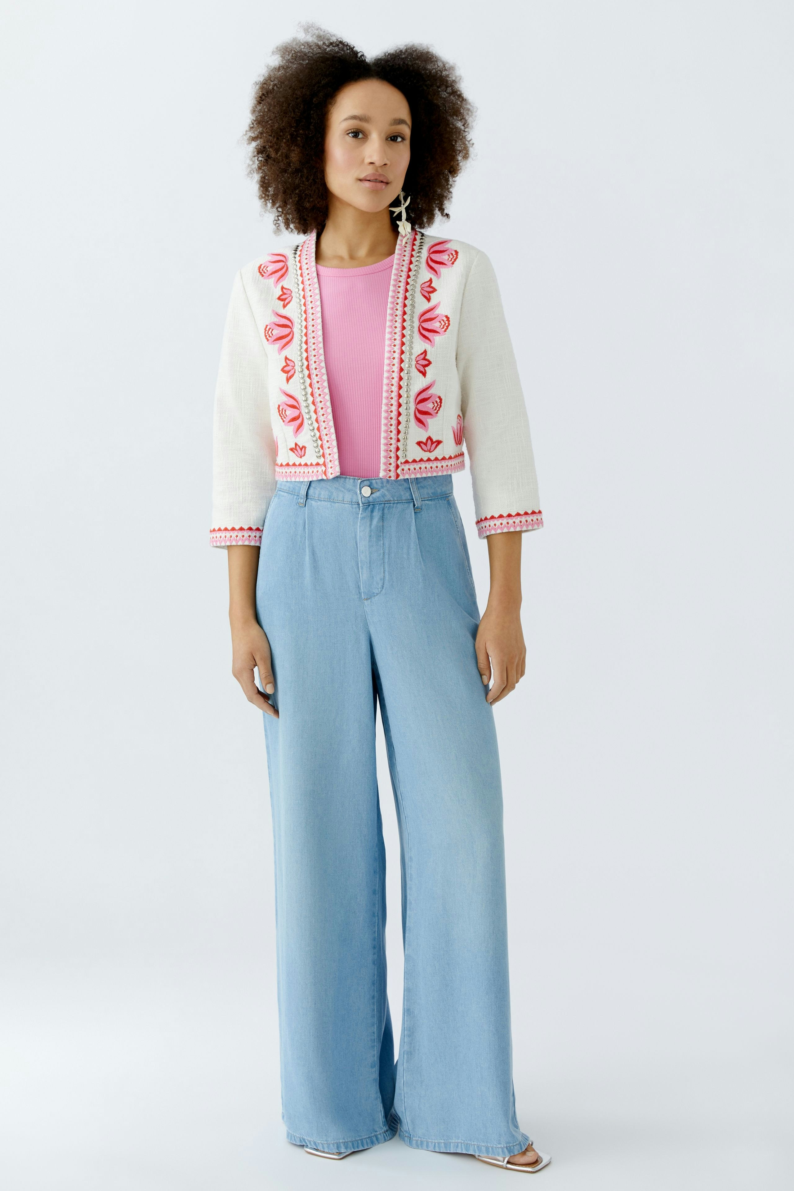 Casual women's jacket: A woman in a white jacket with colorful embroidery over a pink top and wide jeans.