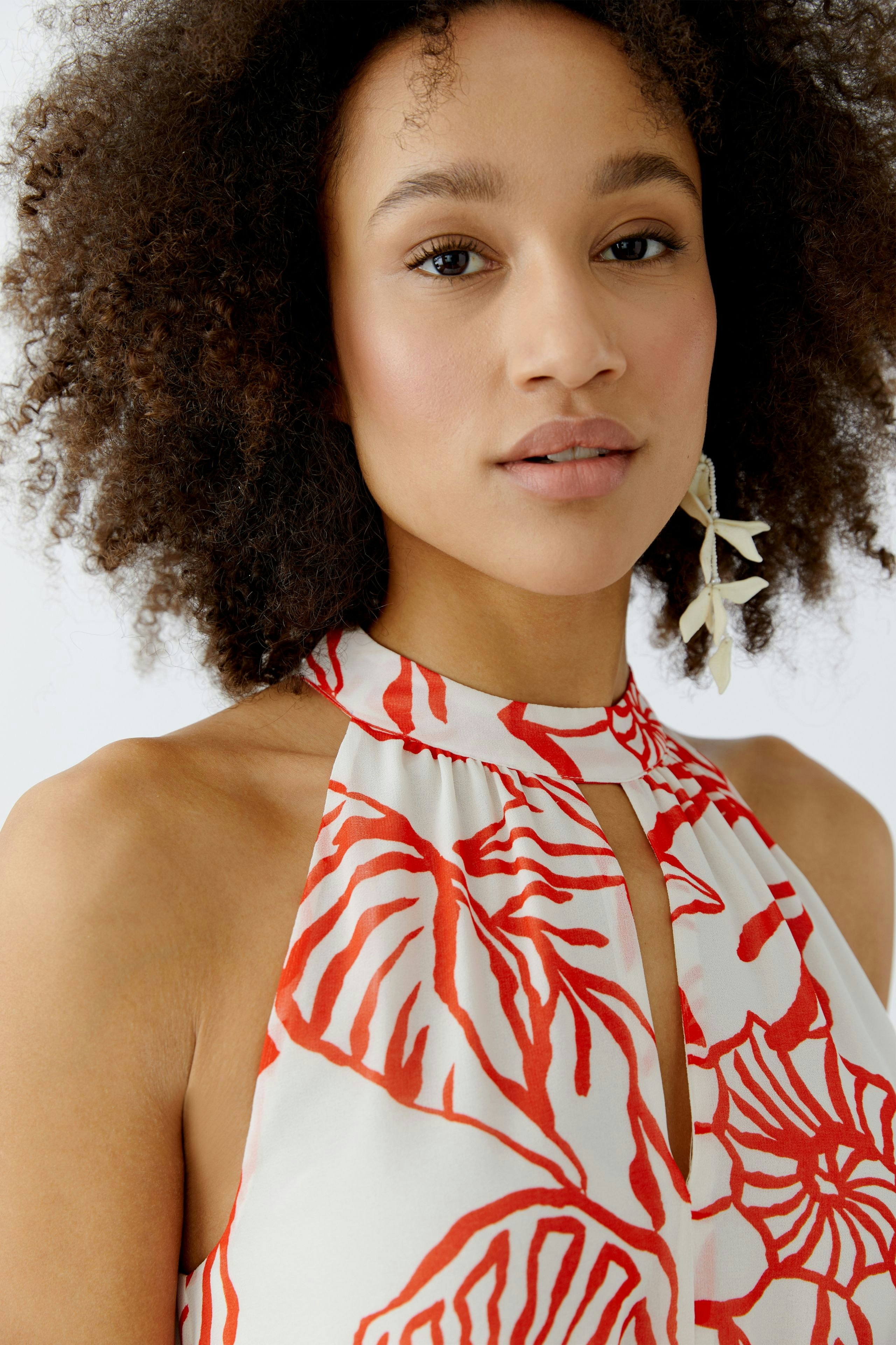 Maxikleid: Frau mit lockigen Haaren trägt ein blumiges Maxikleid mit Halspartie und lässigem Schnitt.