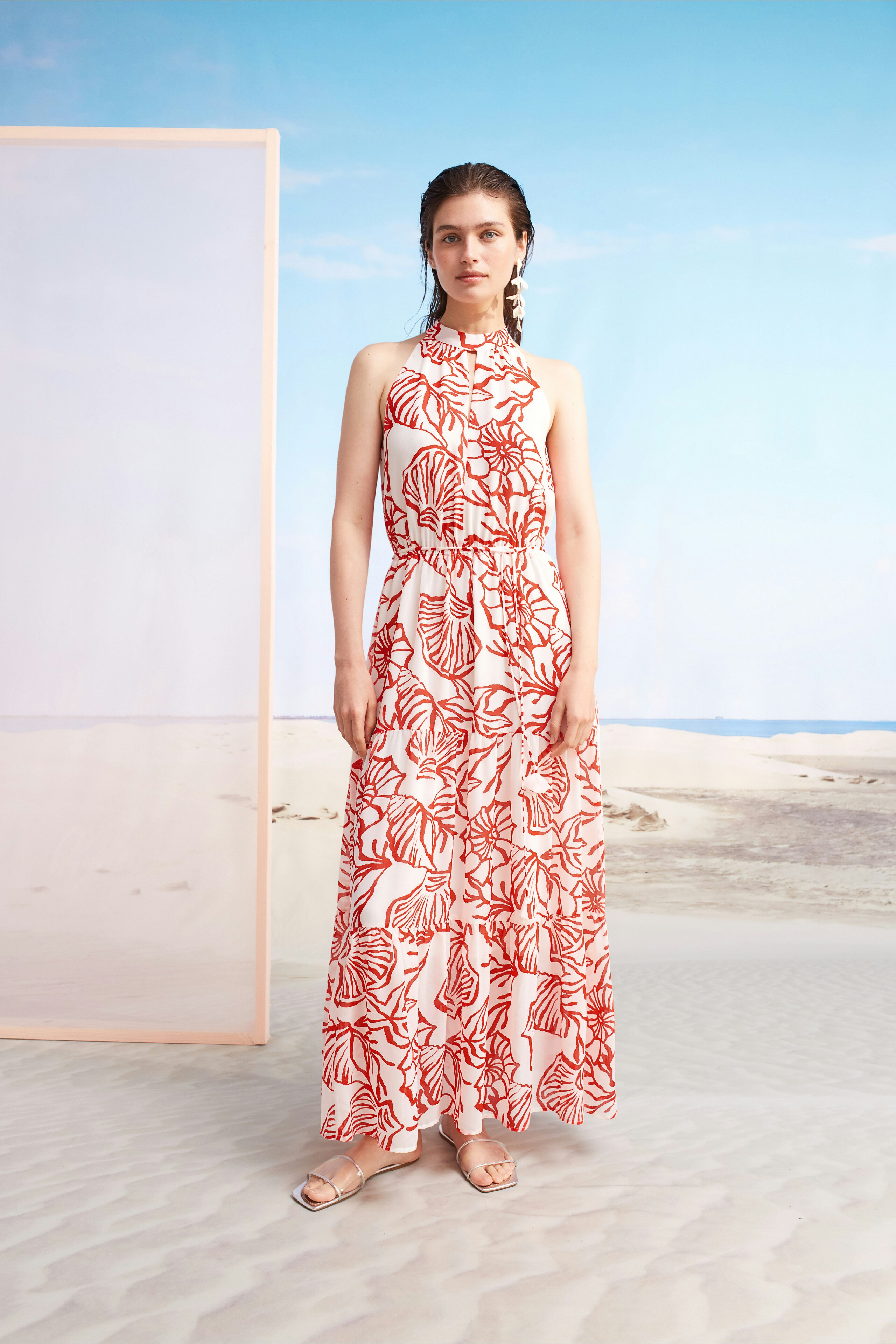 Maxikleid: Frau in einem langen, blumigen Kleid mit hohem Kragen steht am Strand.