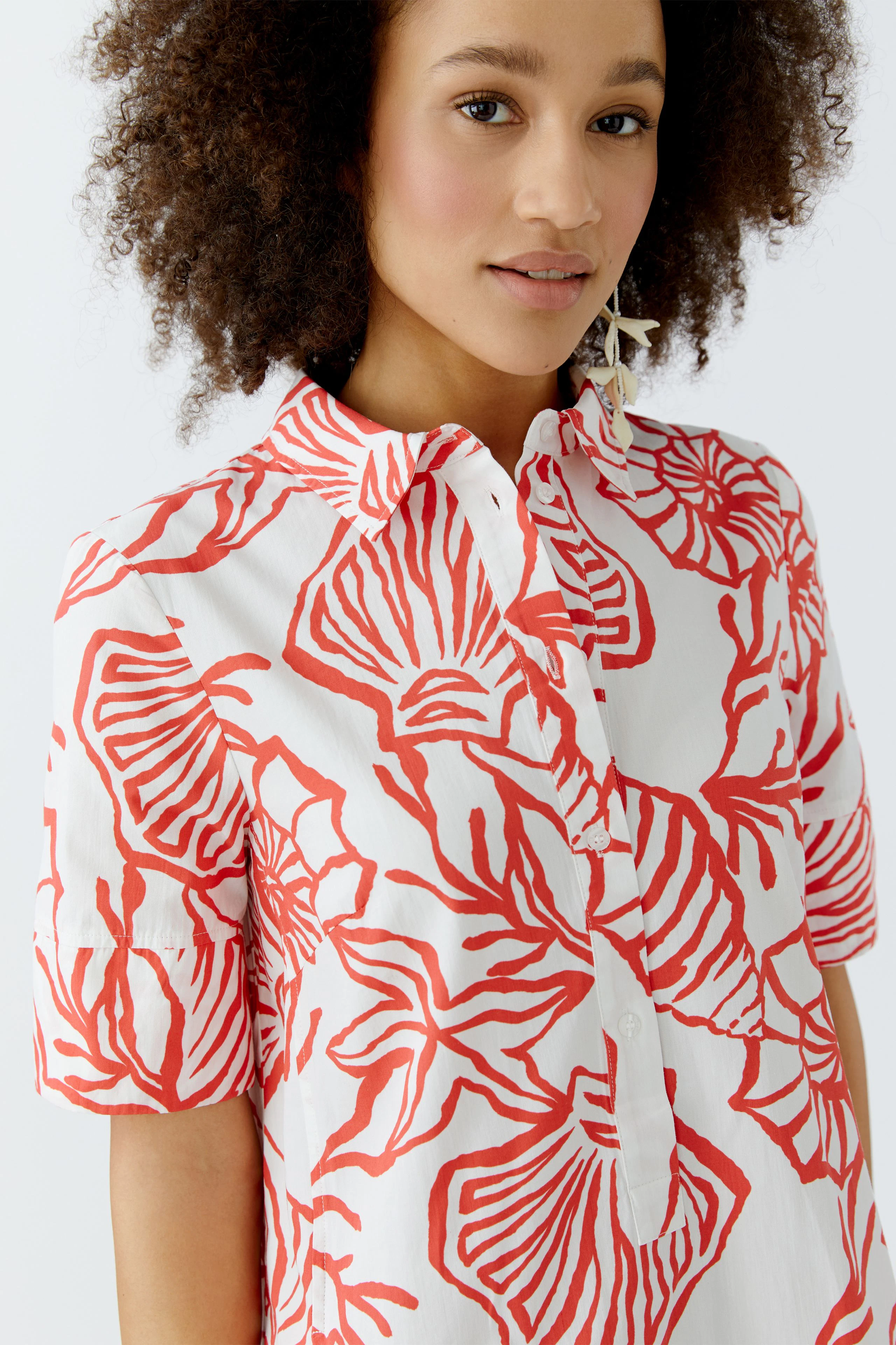 Hemdblusenkleid: Frau mit lockigen Haaren trägt ein blumiges, kurzärmliges Kleid in Rot und Weiß.