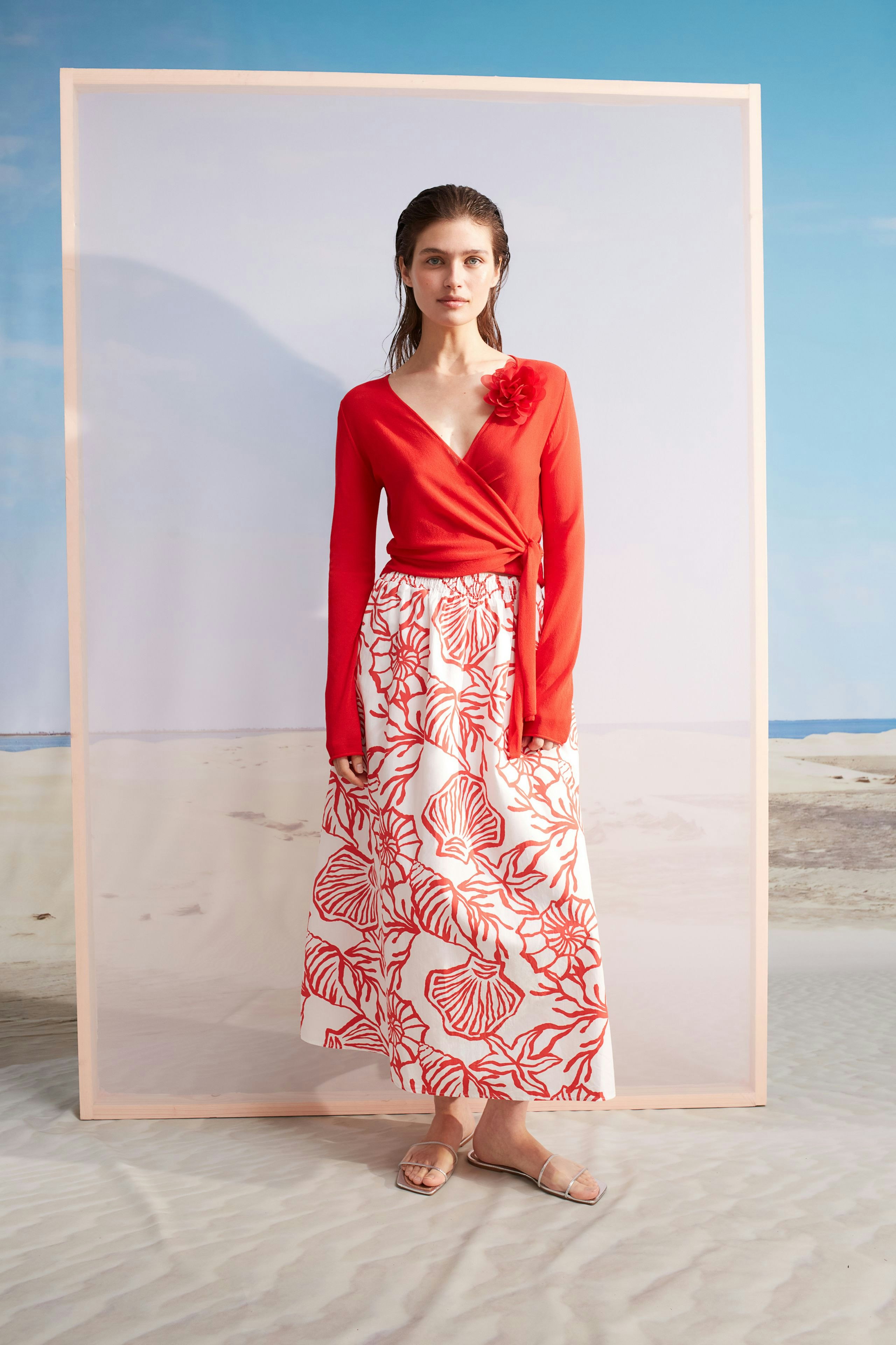 Stylish maxi skirt: Woman in a red top and floral maxi skirt stands confidently against a beach backdrop.