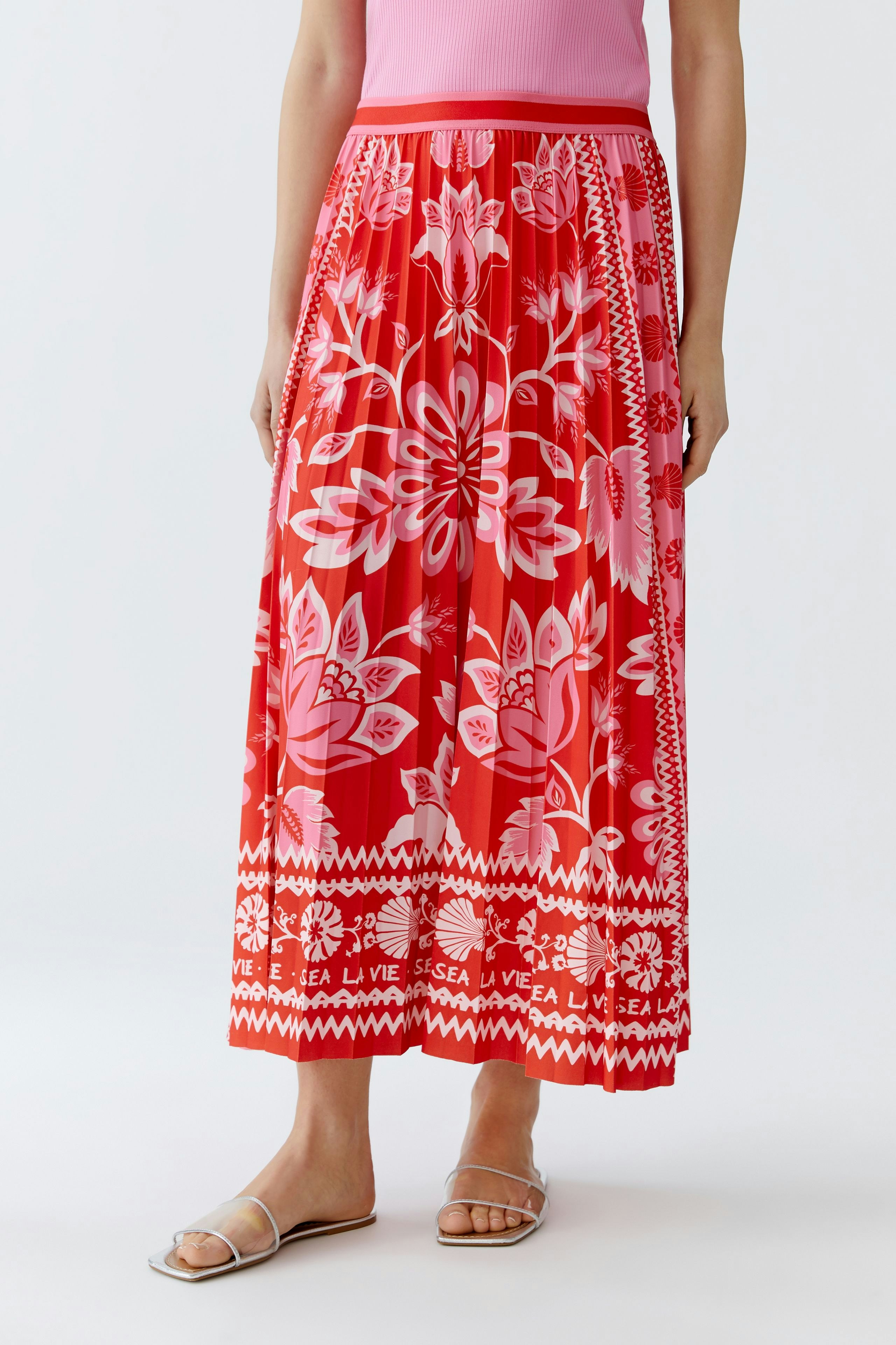 Femininer Plisseerock in Rot mit floralem Muster, kombiniert mit einem pinken Oberteil.