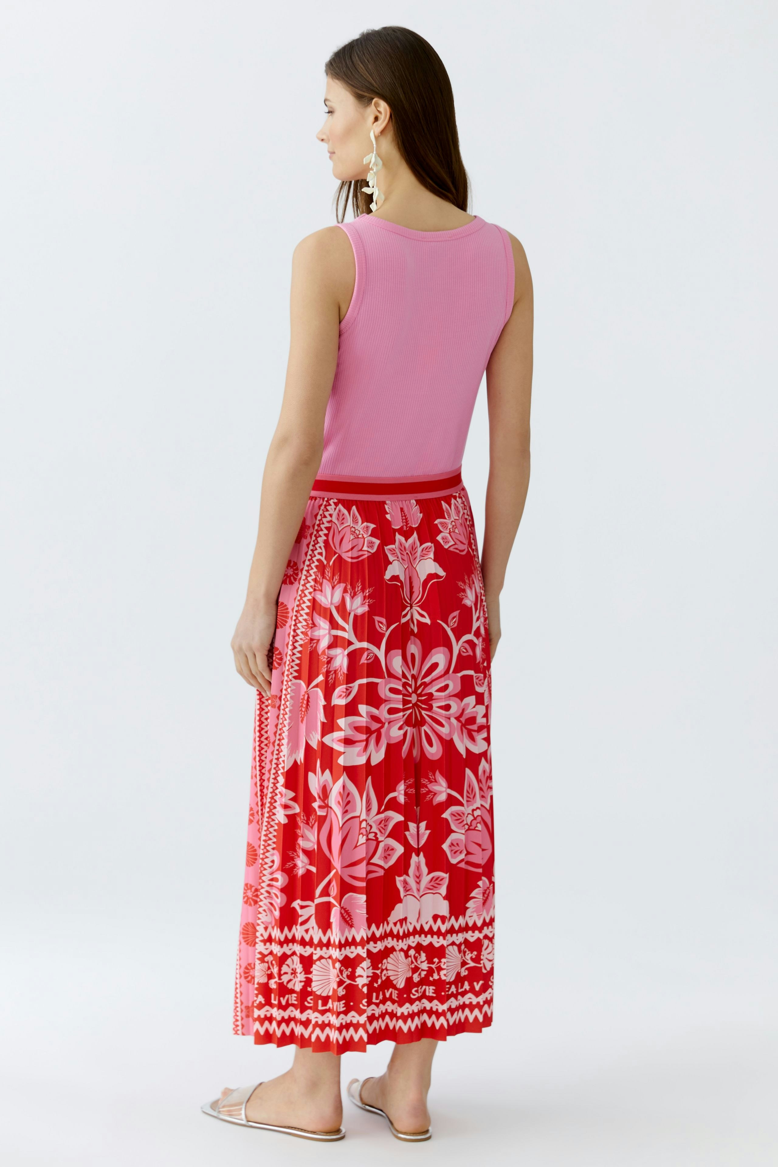 Damen-Plisseerock: Frau trägt einen farbenfrohen Rock mit floralem Muster und lässigem Oberteil.