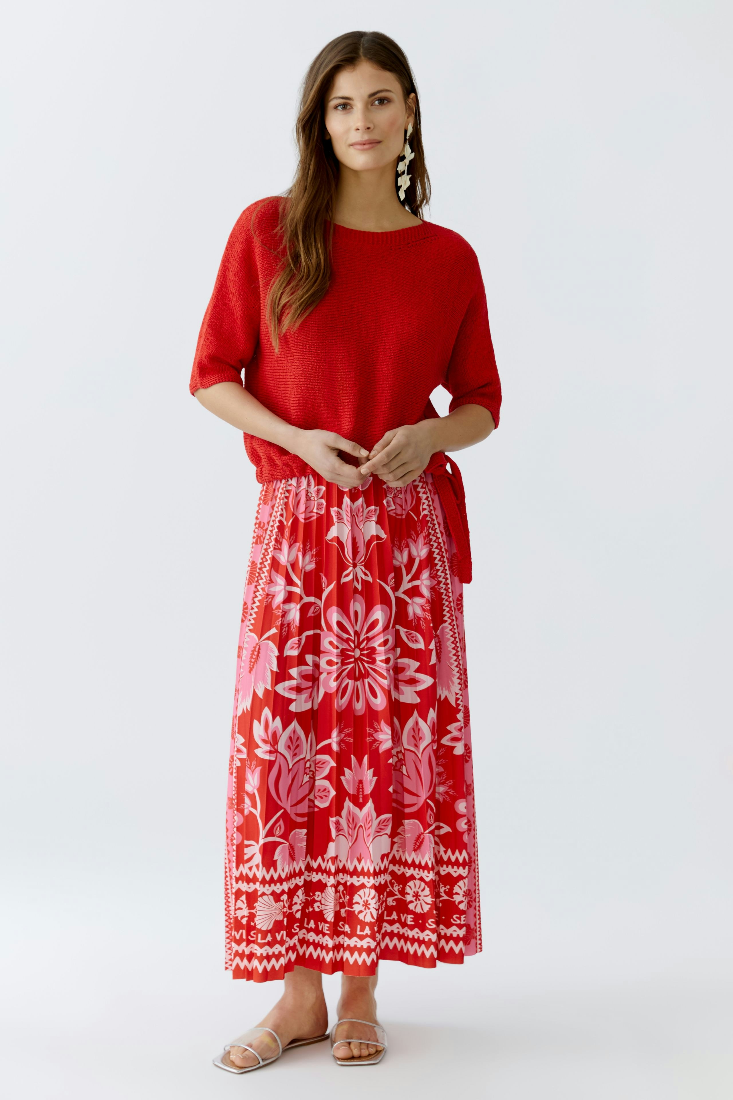 Frau in buntem Plisseerock mit floralem Muster und rotem Oberteil, lässig und modern.