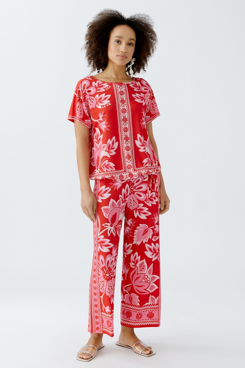Damen-T-Shirt: Frau in rotem, floralem T-Shirt mit lässigem Schnitt und passender Hose.