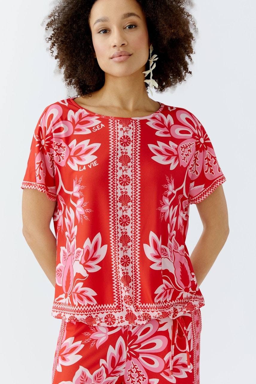 Damen-T-Shirt: Frau trägt ein rotes, floral gemustertes T-Shirt mit Rundhalsausschnitt und lockerer Passform.