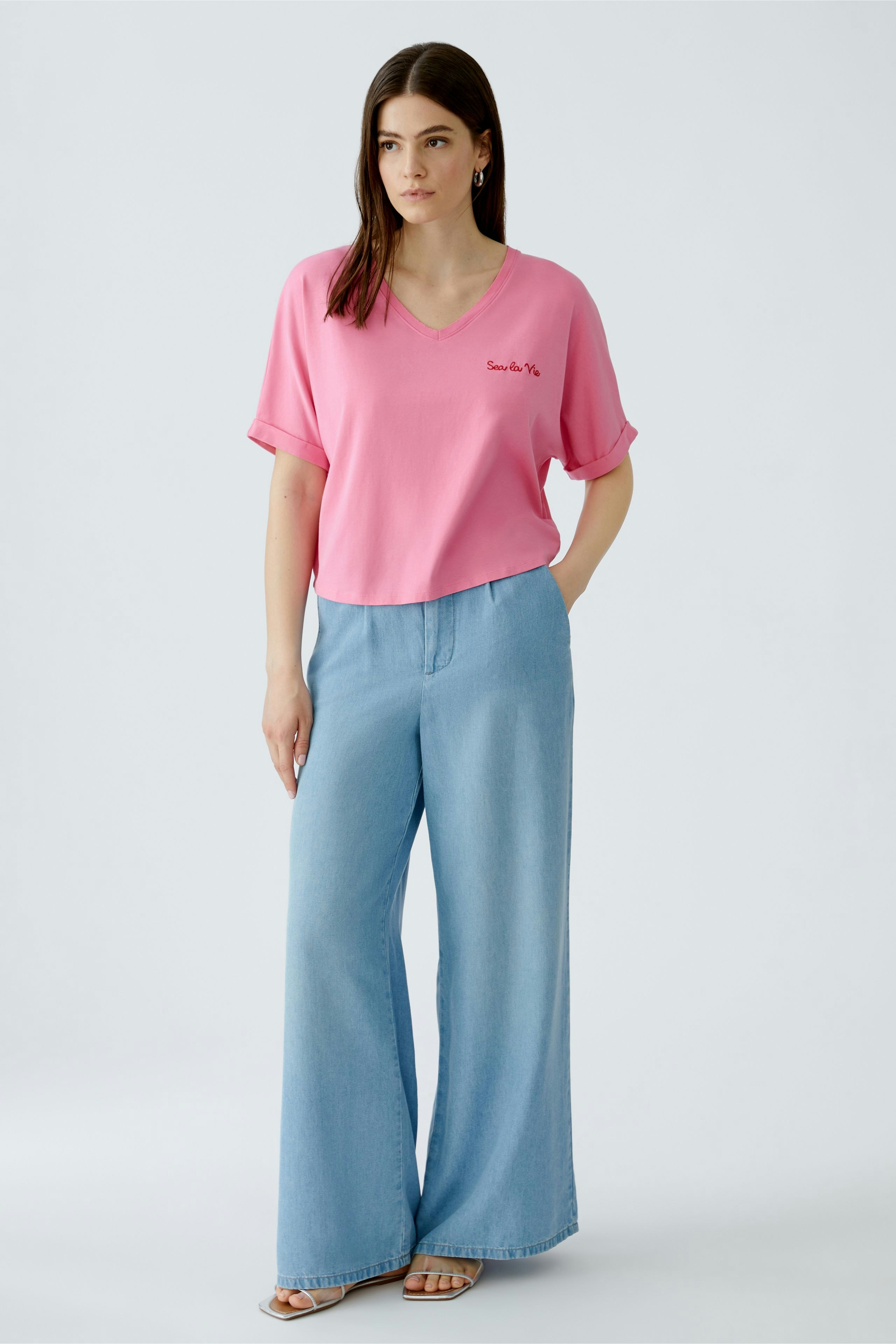 Casual women's T-shirt: Young woman in a pink V-neck tee with rolled sleeves and relaxed fit.