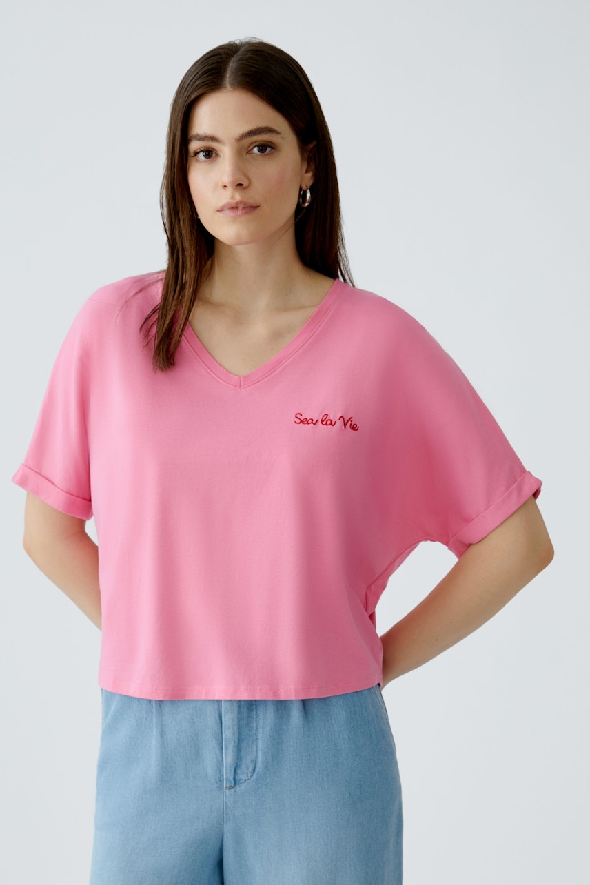 Casual women's T-shirt: Young woman in a pink V-neck tee with rolled sleeves, featuring a logo.