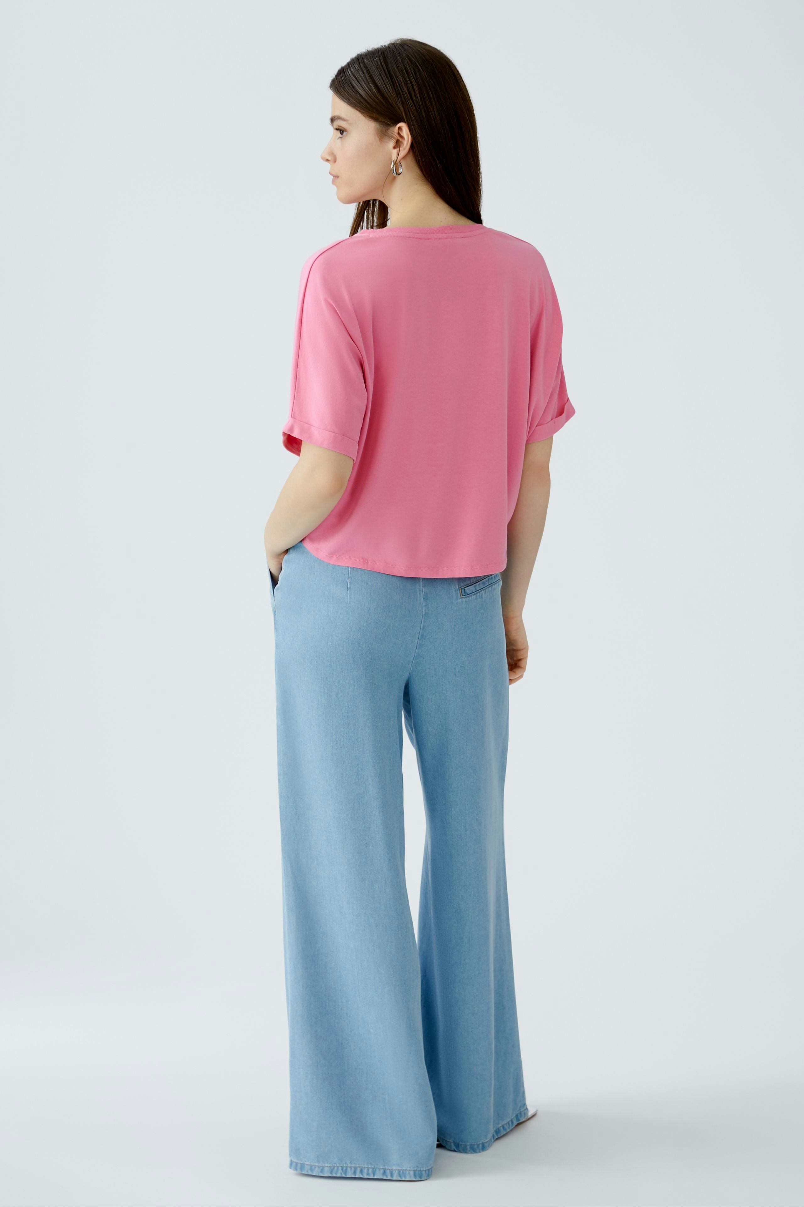 Casual women's T-shirt: Young woman in a pink top paired with wide-leg jeans, showcasing a relaxed style.