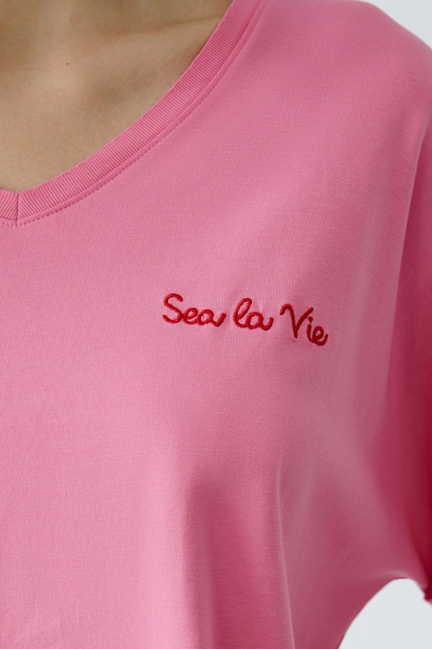Casual women's T-shirt: Close-up of a woman in a pink tee with 'Sea la Vie' embroidered in red.