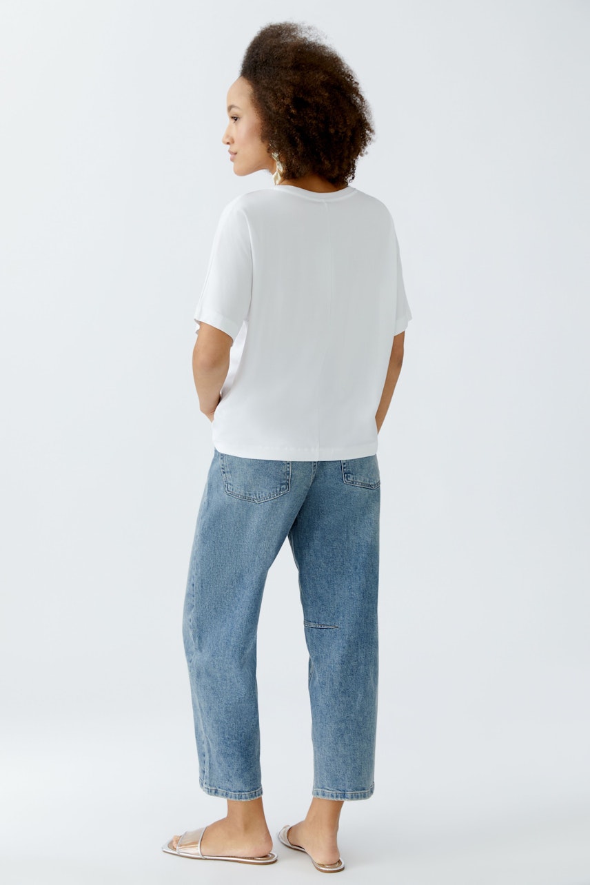 Lässiges Damen-T-Shirt: Frau mit lockigen Haaren trägt ein weißes T-Shirt und bequeme Jeans.