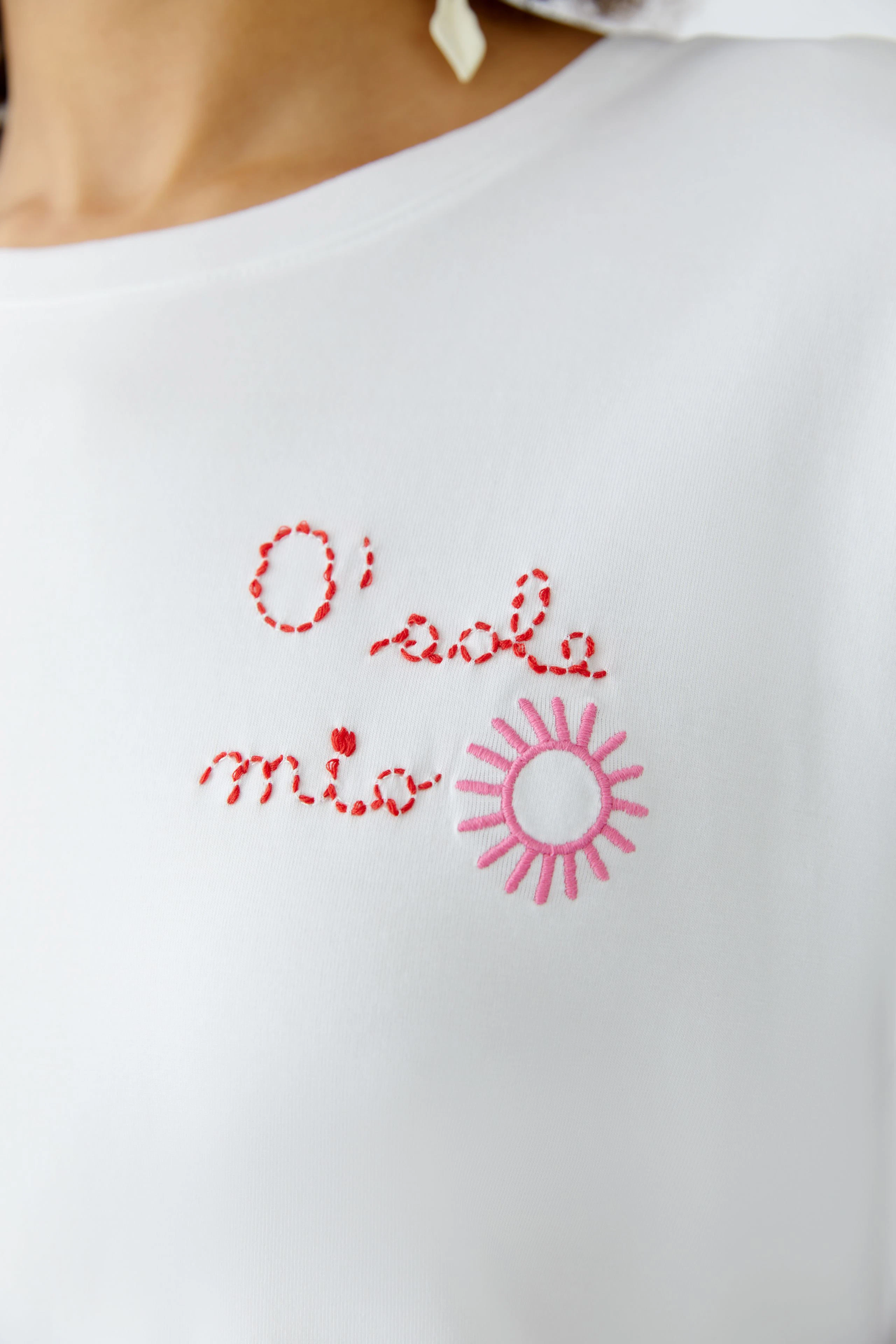 Casual women's T-shirt: Close-up of a woman in a white tee with colorful embroidery and a cheerful sun design.