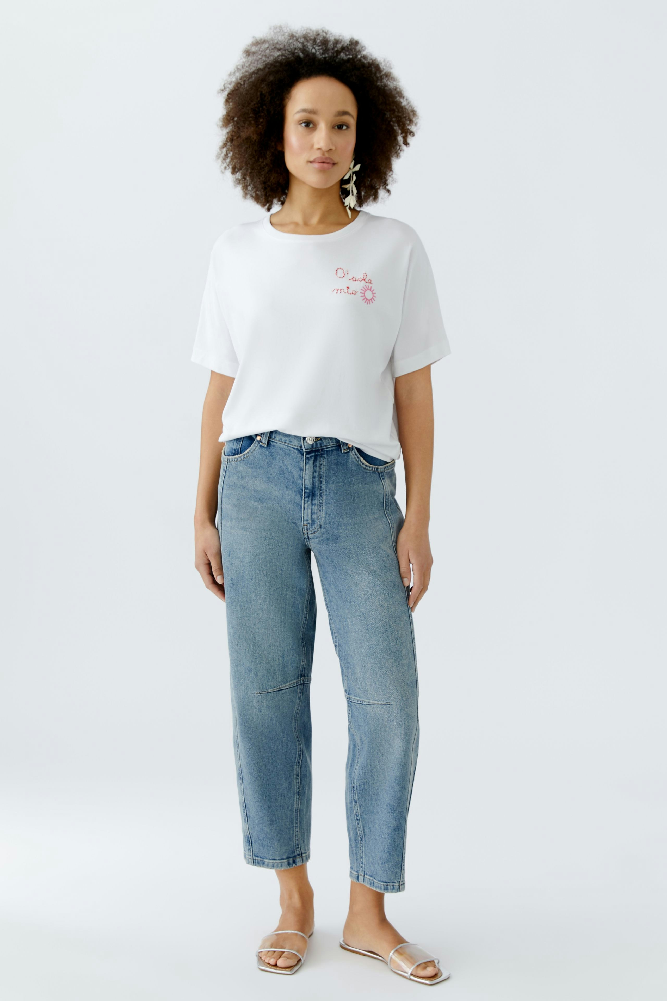 Damen-T-Shirt: Frau trägt ein weißes T-Shirt mit pinkem Aufdruck und kombiniert es mit lässigen Jeans.