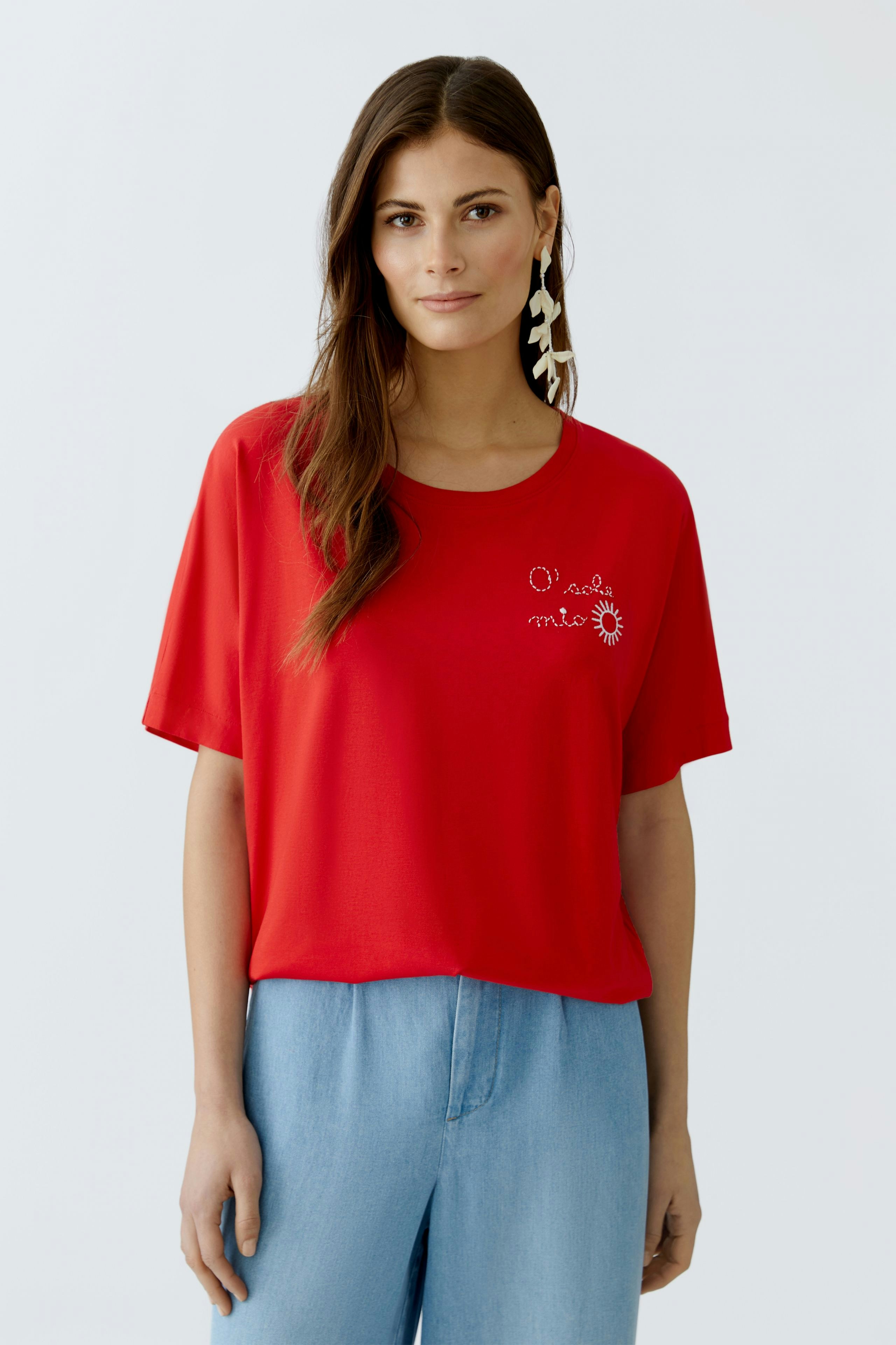 Casual women's T-shirt: Young woman in a red tee with a playful print, paired with light blue pants.
