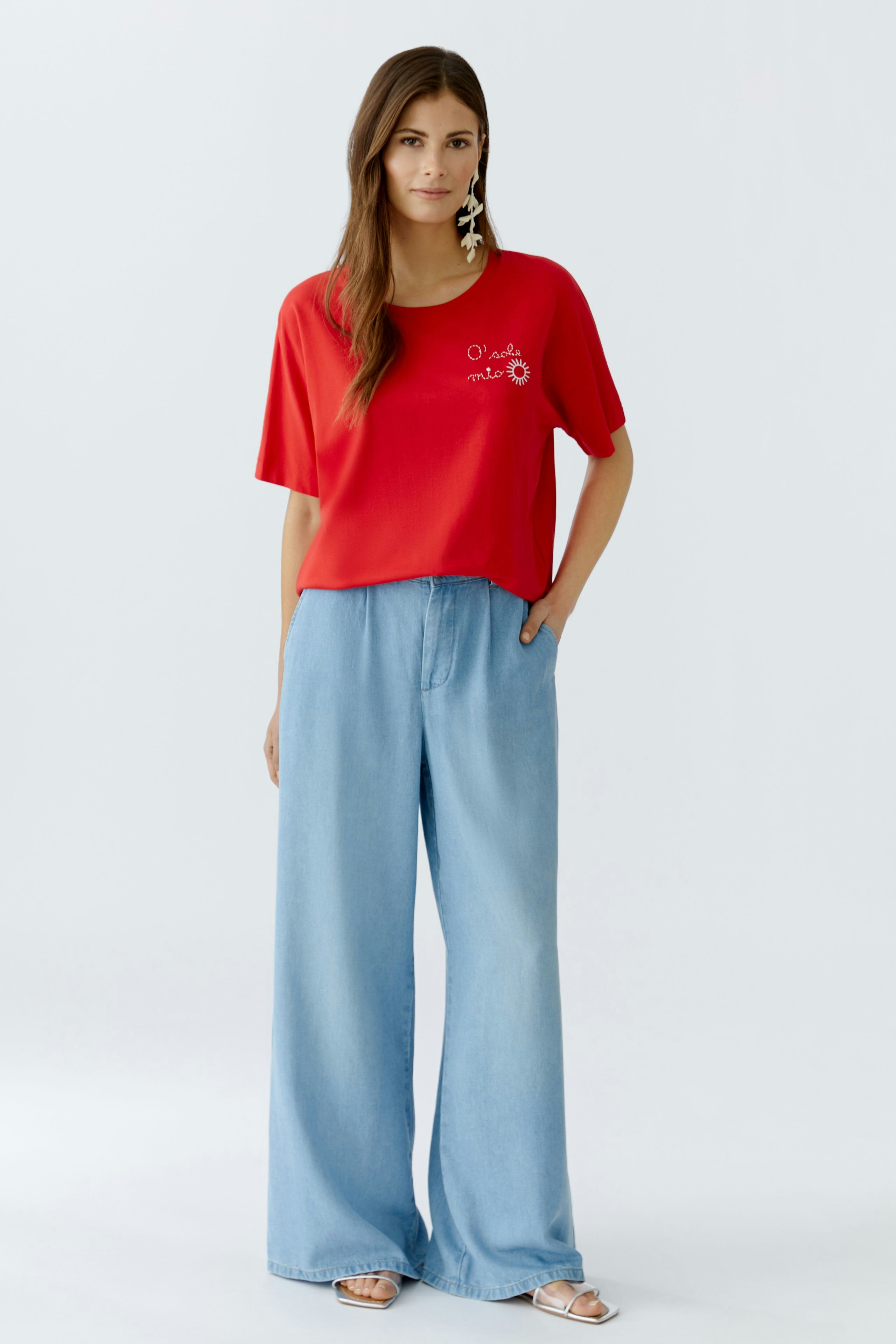 Casual women's T-shirt: Young woman in a red T-shirt with a graphic design and wide blue pants.
