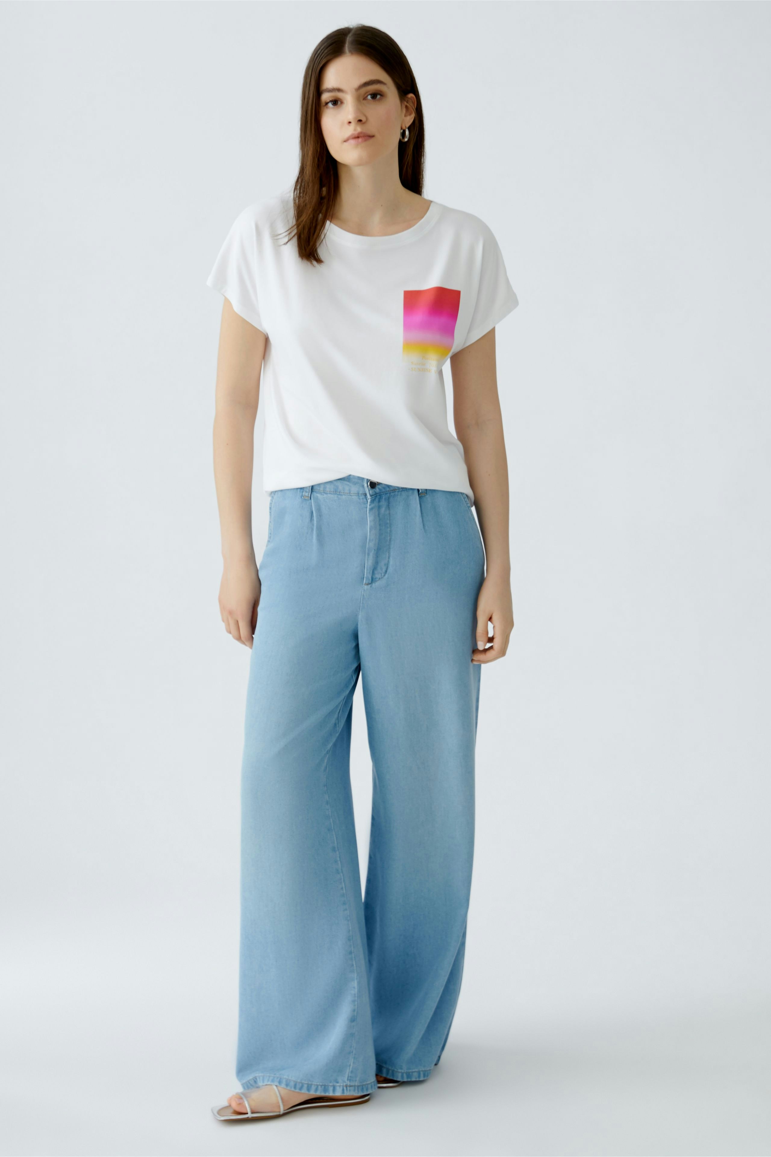 Casual women's T-shirt: Young woman in a white tee with a colorful pocket design, paired with wide-leg jeans.
