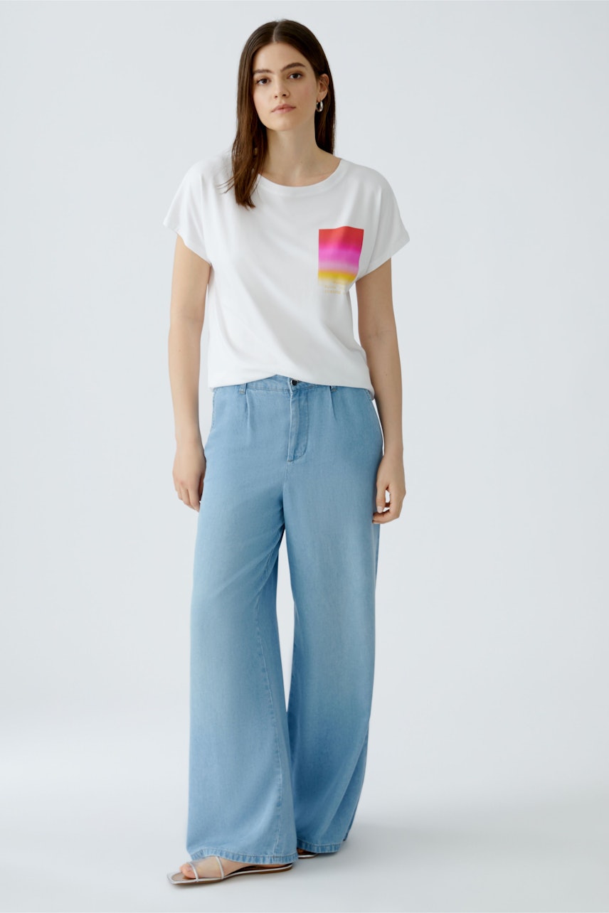 Casual women's T-shirt: Young woman in a white tee with a colorful pocket design, paired with wide-leg jeans.