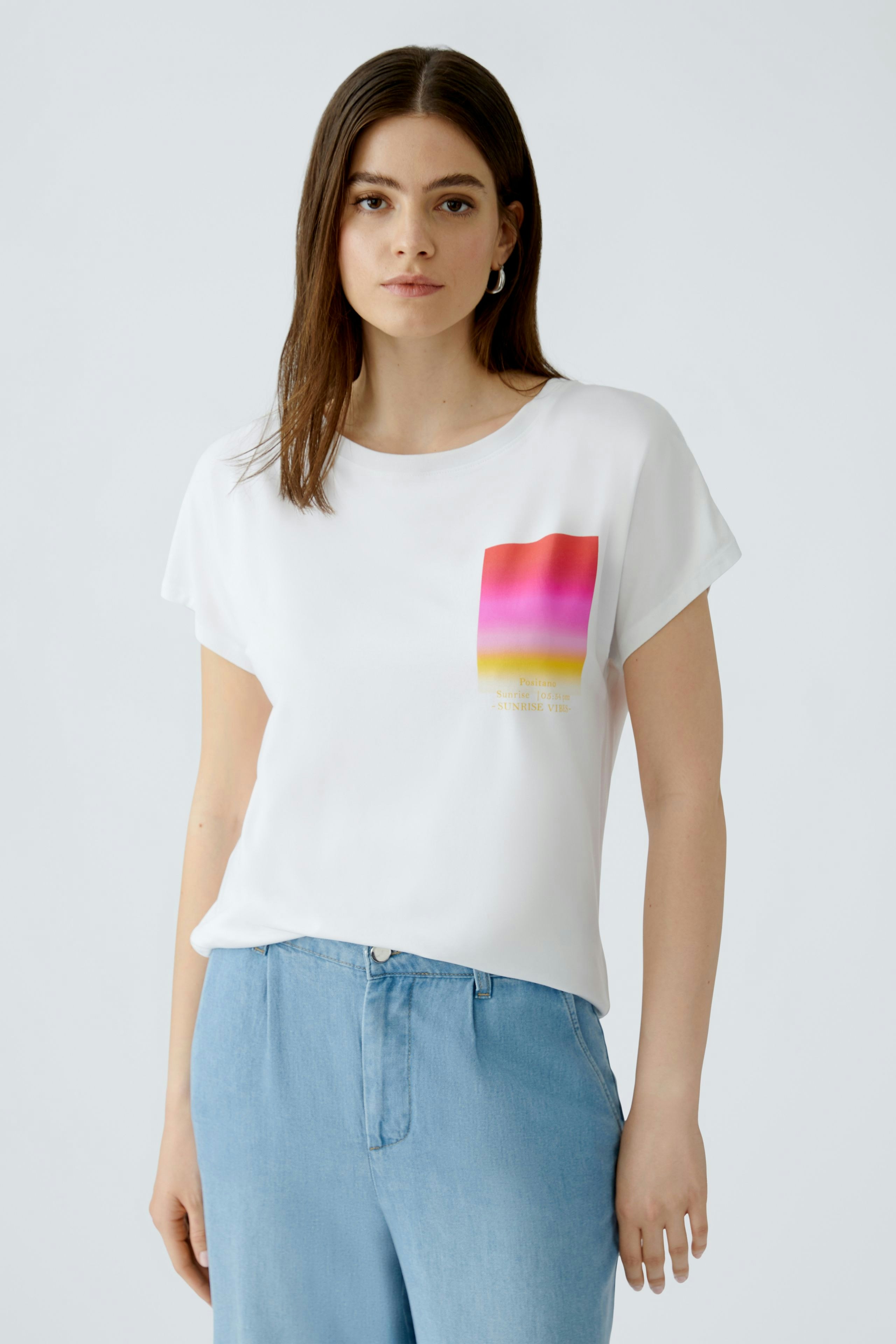 Casual women's T-shirt: Young woman in a white tee with a colorful graphic design, paired with light blue pants.