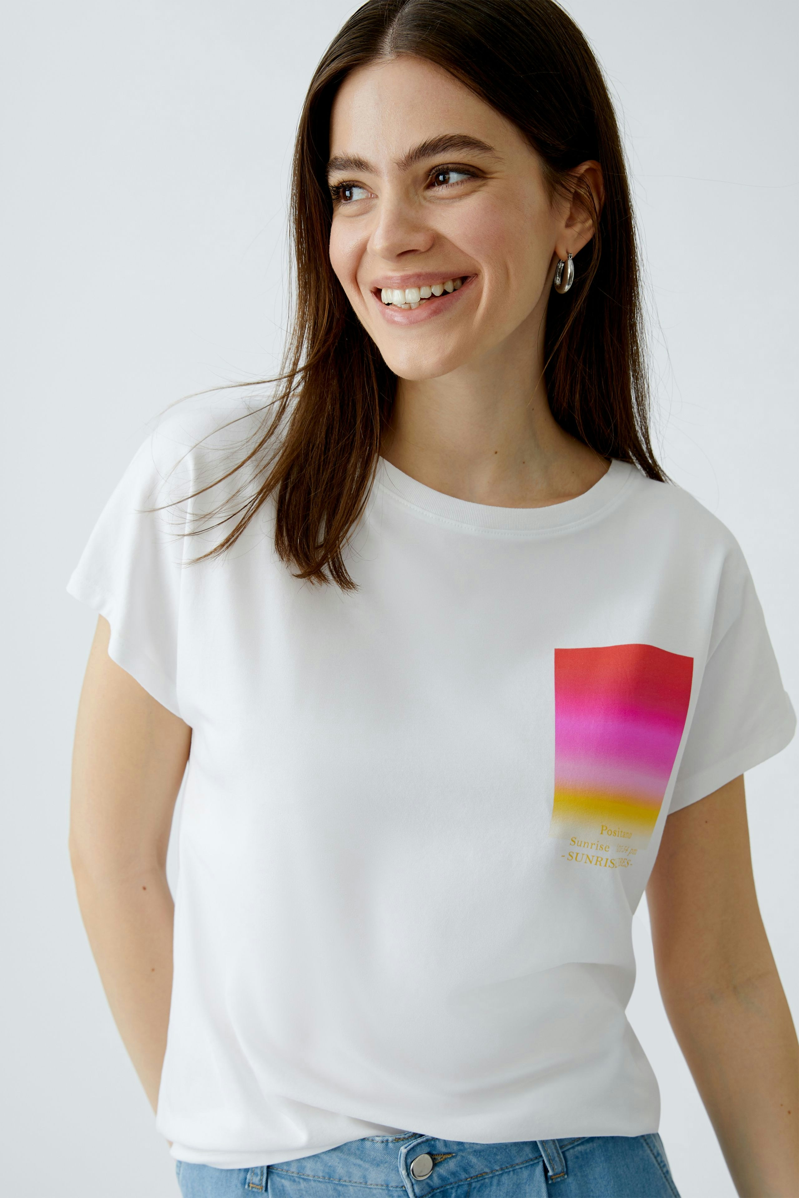 Casual women's T-shirt: Smiling woman in a white tee with colorful graphic and rolled sleeves.