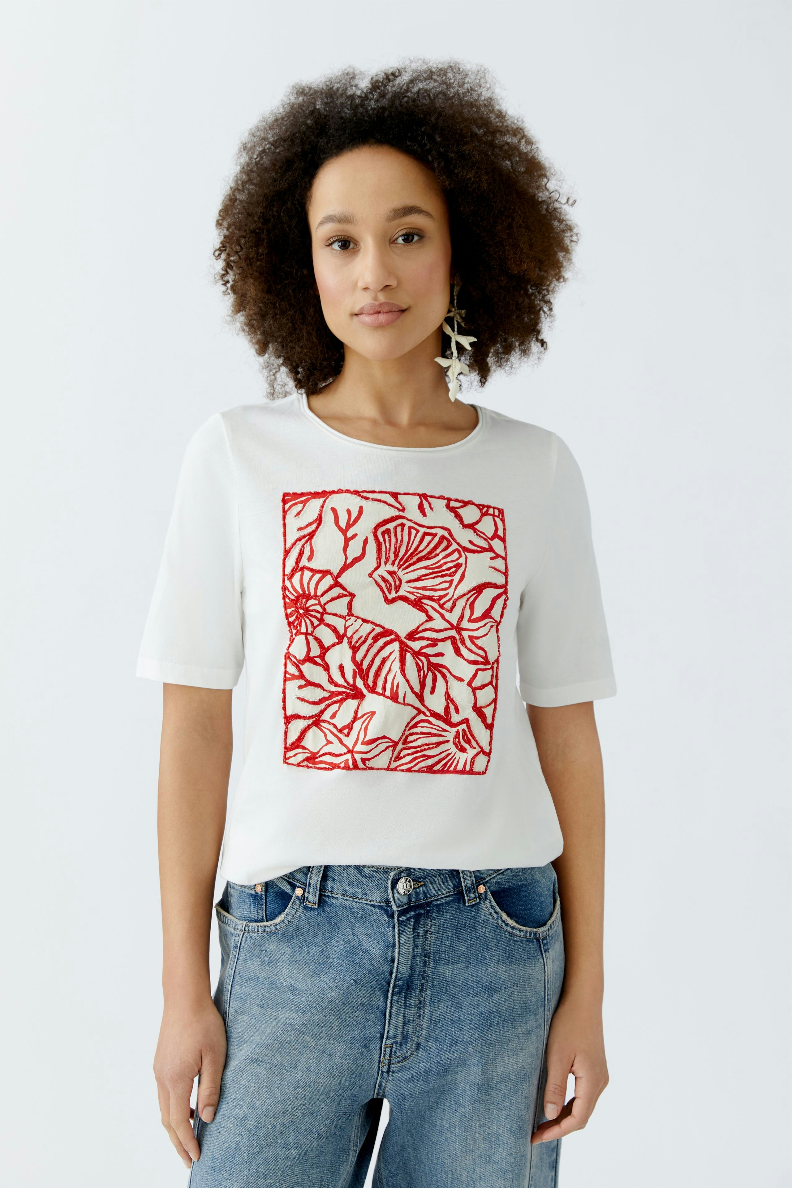 Damen-T-Shirt: Frau trägt ein weißes T-Shirt mit rotem Blumenmuster und lässigen Jeans.