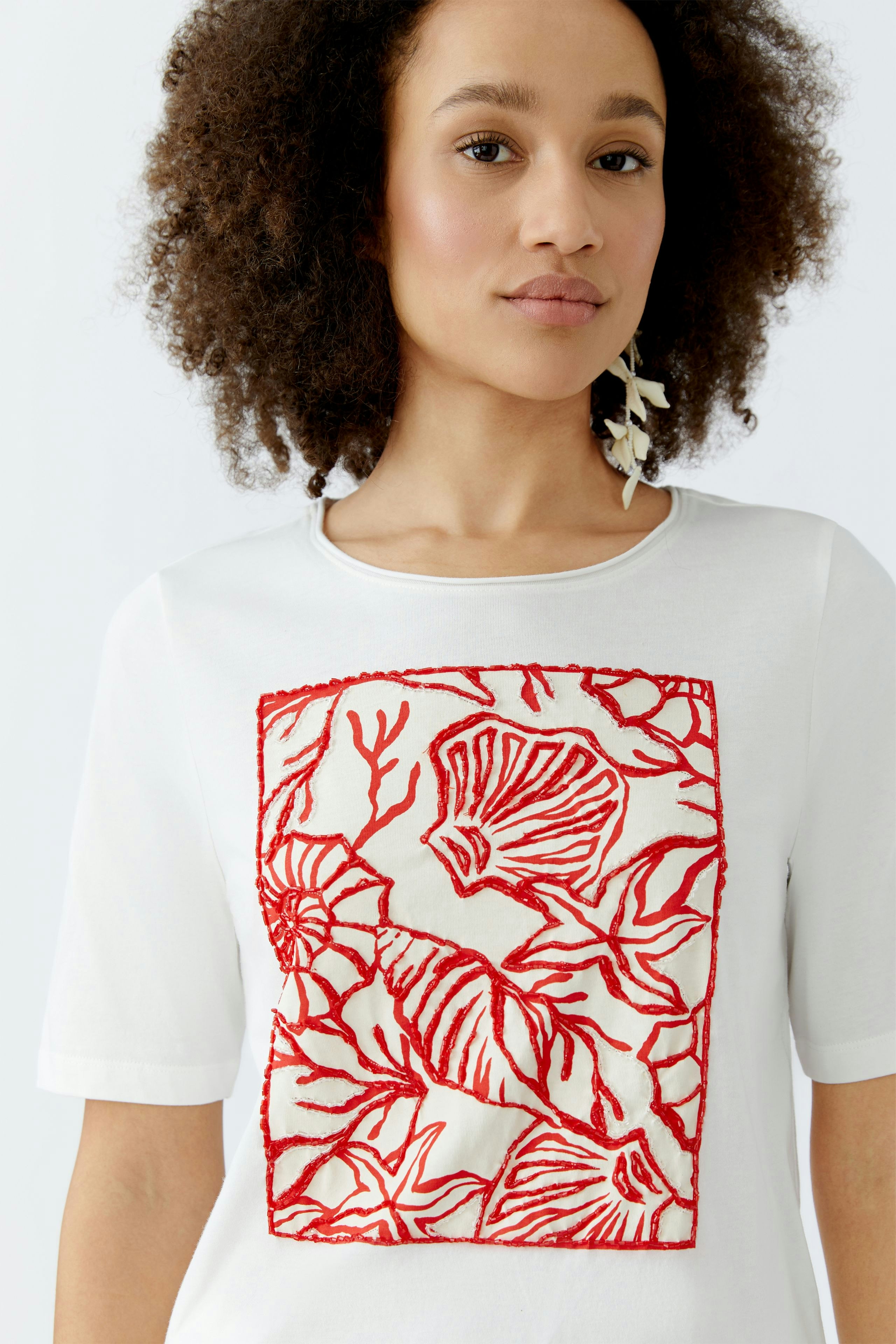Damen-T-Shirt: Frau trägt ein weißes T-Shirt mit rotem, floralem Stickmuster.