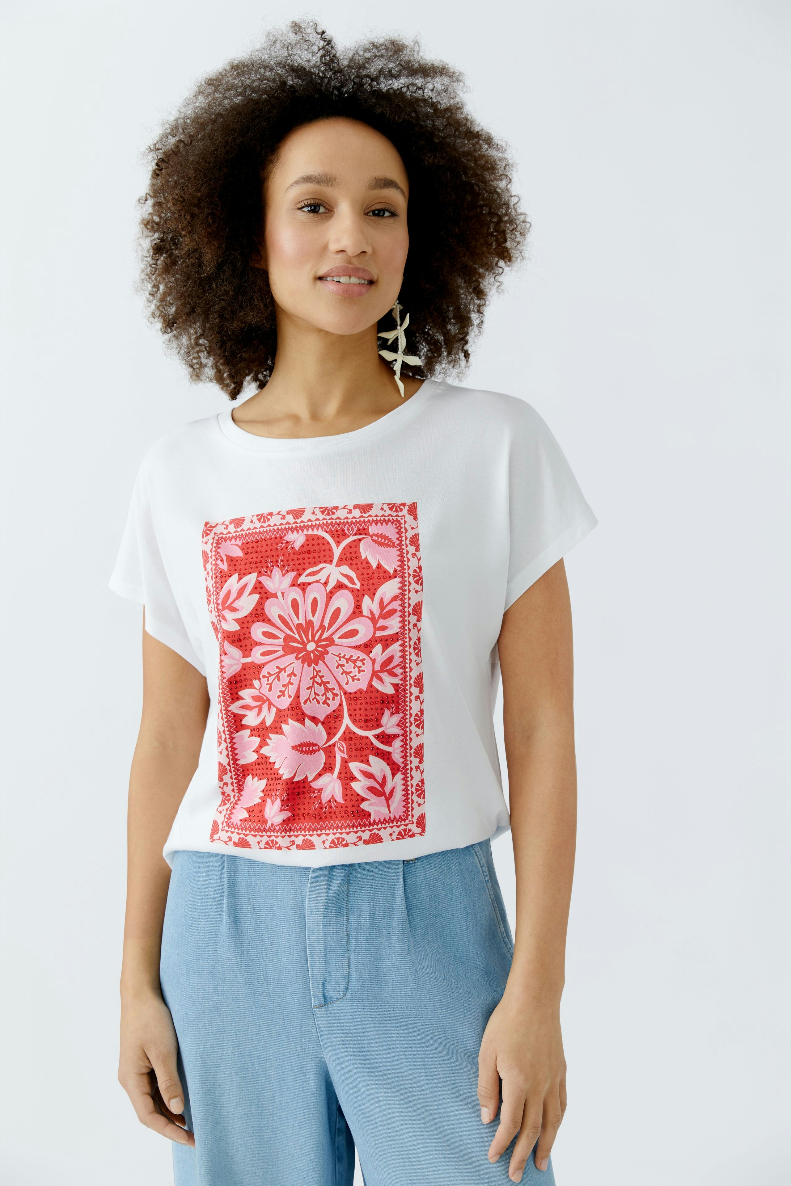 Casual women's T-shirt: Woman in a white tee with a colorful floral print, paired with light blue pants.