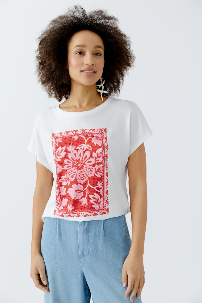 Damen-T-Shirt: Frau trägt ein weißes T-Shirt mit rotem Blumenmuster und lässigen Jeans.