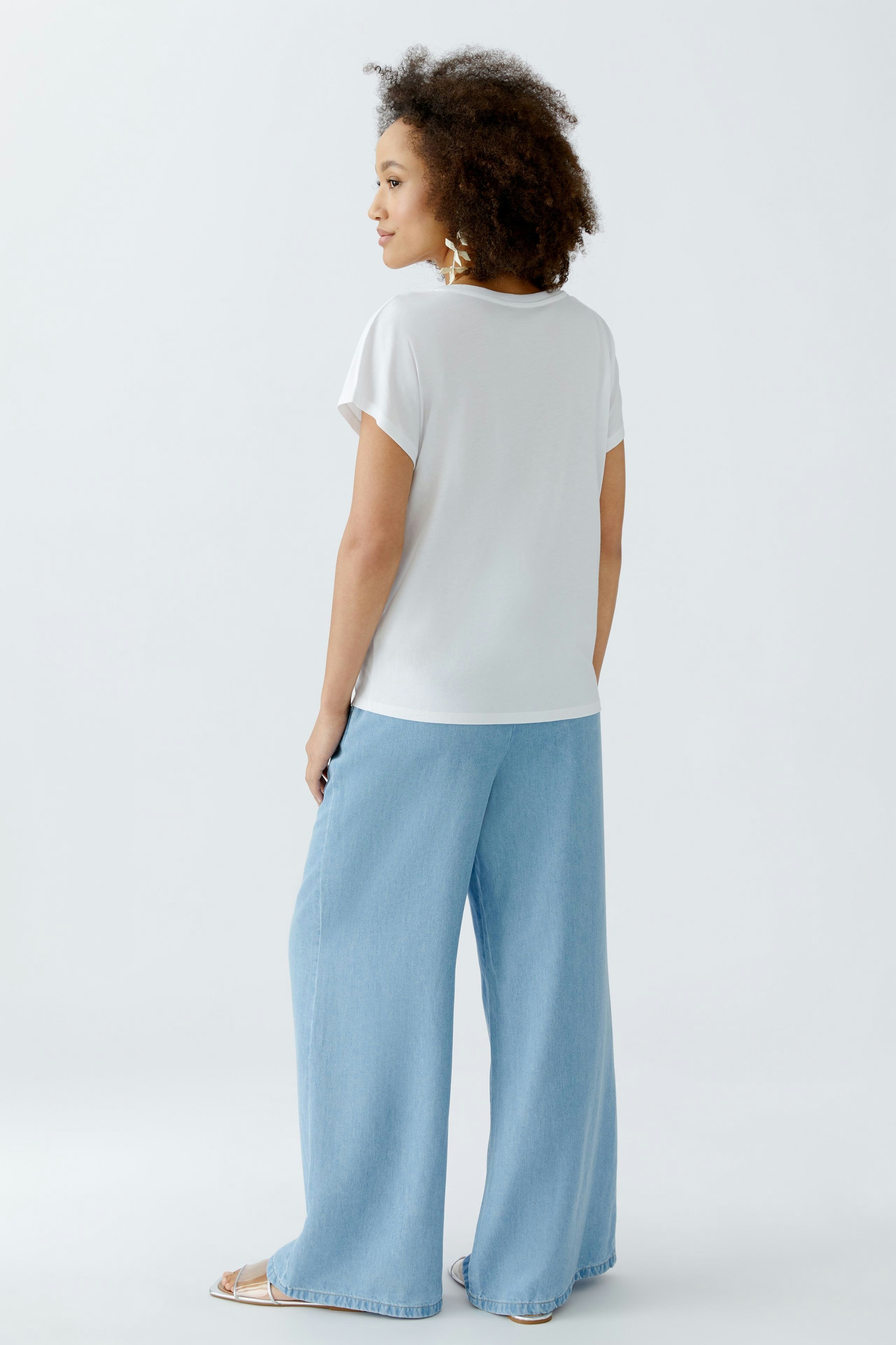 Casual women's T-shirt: Woman in a white tee paired with light blue wide-leg pants, showcasing a relaxed style.