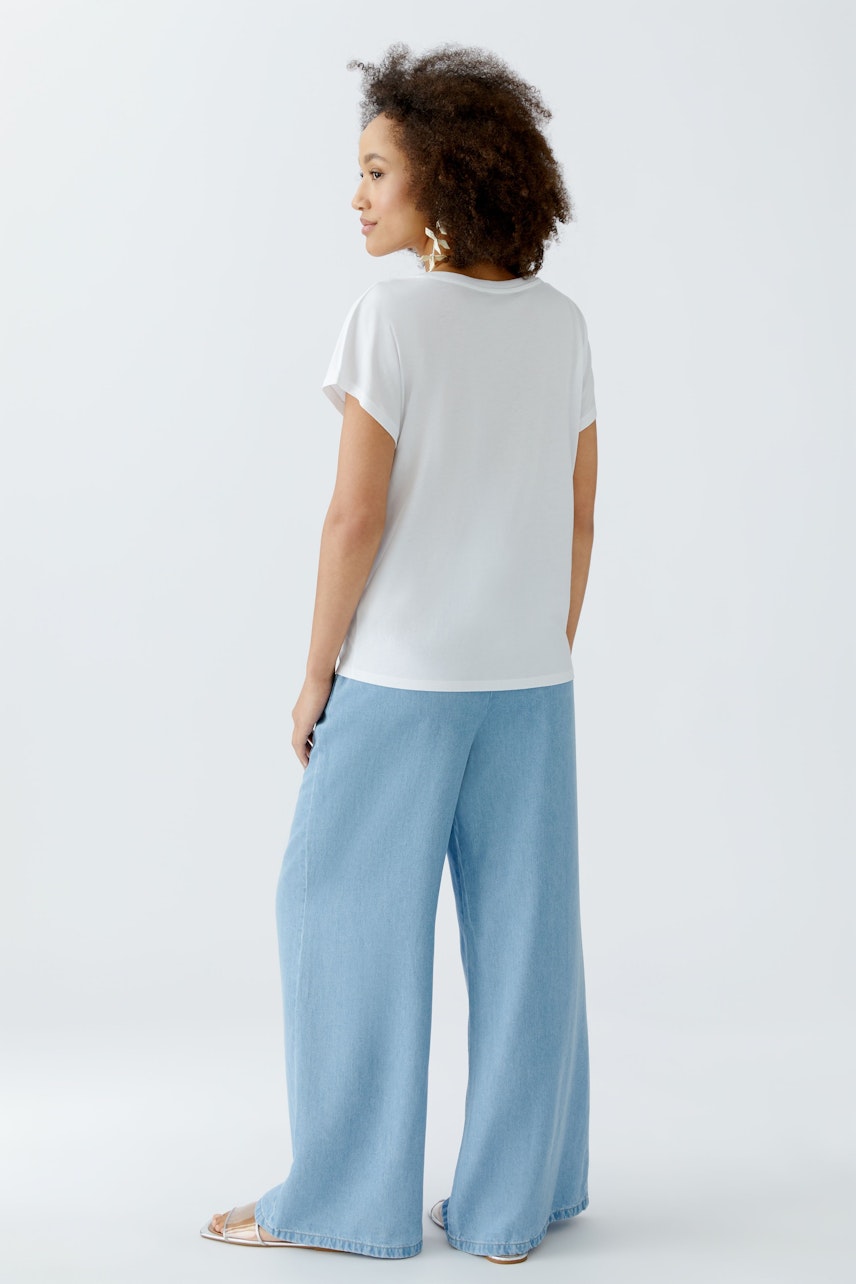 Damen-T-Shirt: Frau trägt ein schlichtes, weißes T-Shirt mit kurzen Ärmeln und lässigen, weiten Jeans.