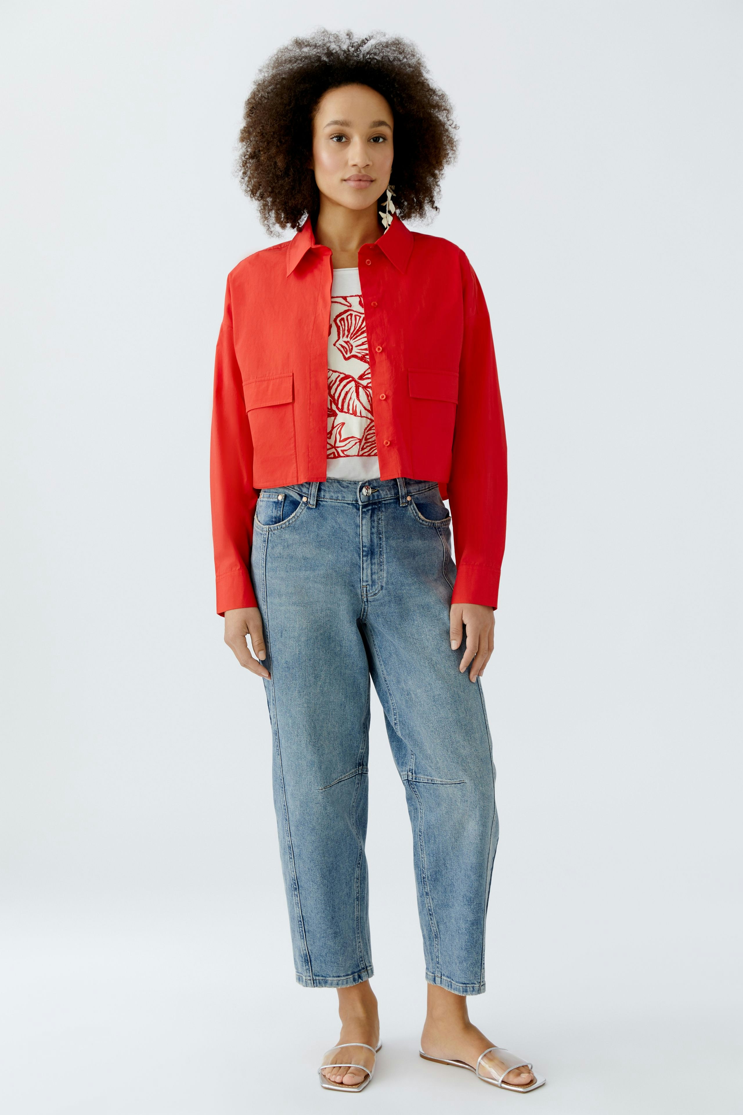 Moderne Damen-Bluse: Frau in roter Bluse mit zwei Taschen und lässigen Jeans steht entspannt.