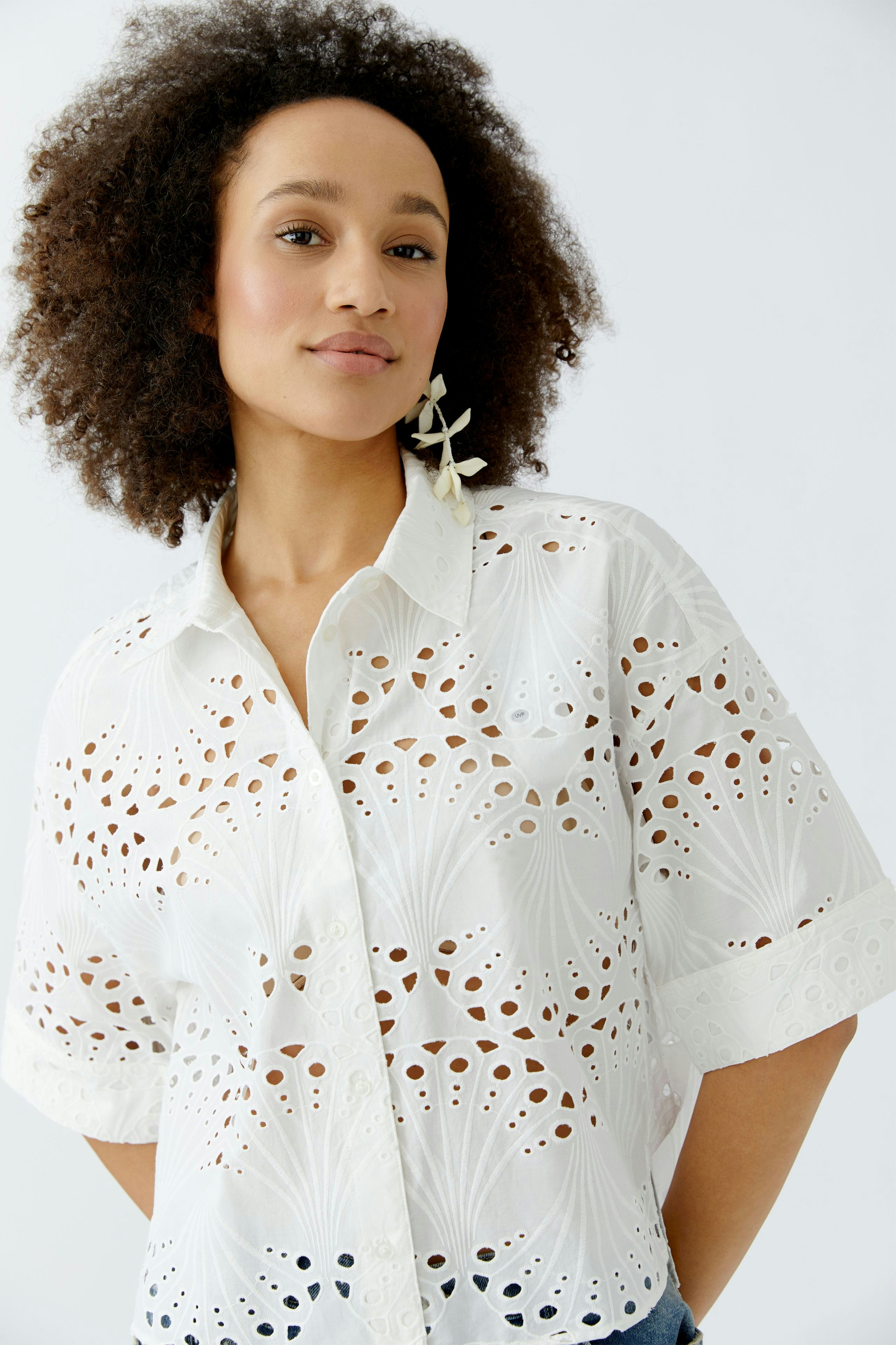 Stylish women's blouse: A woman in a white blouse with intricate cut-out designs, smiling confidently.