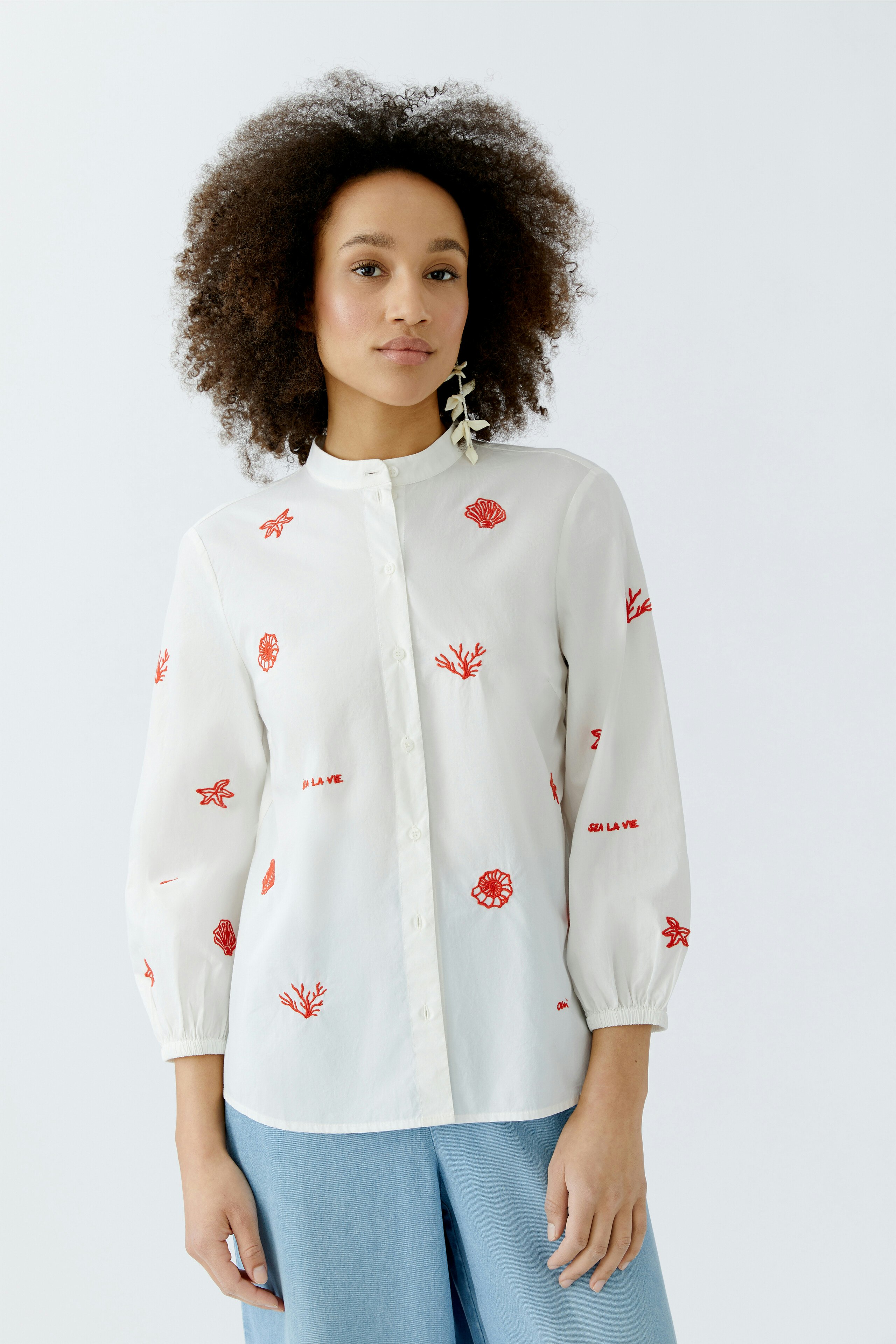 Damen-Bluse: Frau in weißer Bluse mit roten Stickereien und lässigem Schnitt.