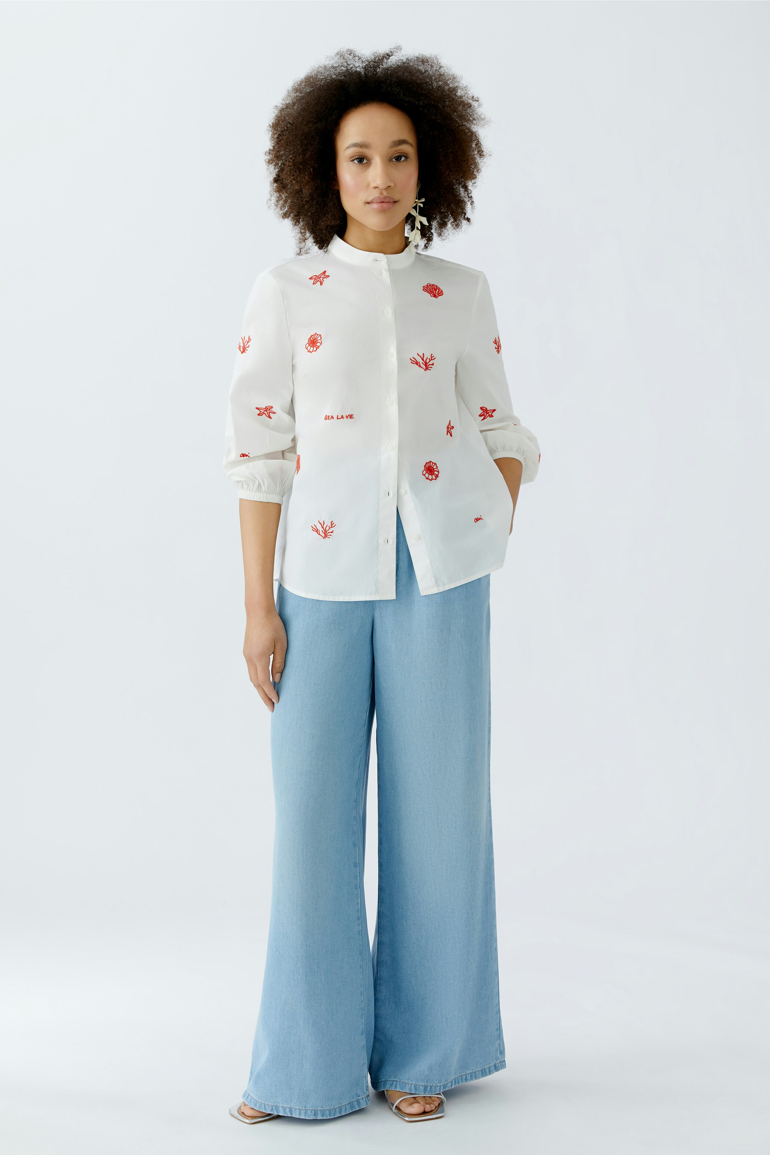 Helle Damen-Bluse mit floralem Muster, kombiniert mit weiten Jeans, getragen von einer Frau.