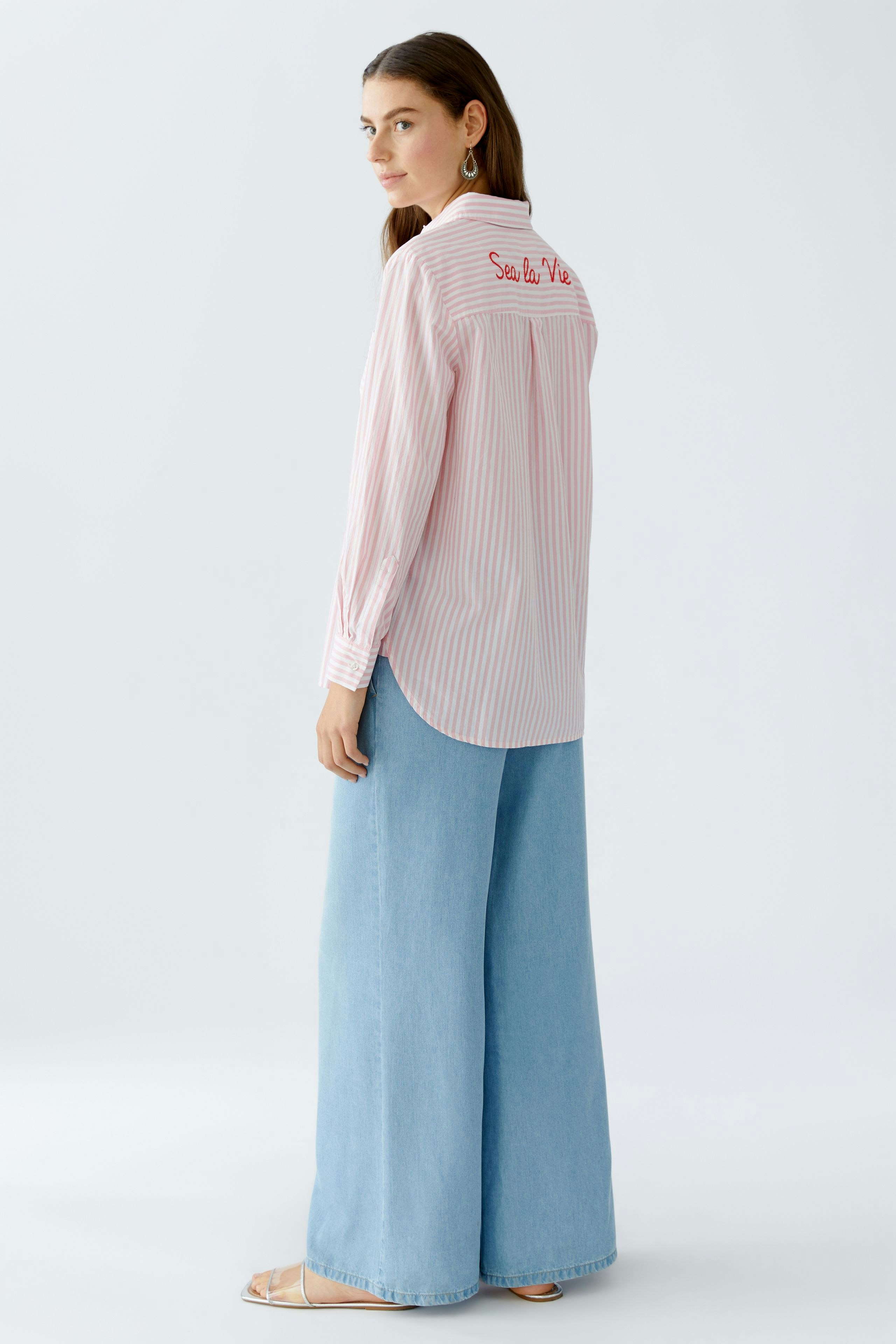 Lässige Hemdbluse: Frau trägt eine gestreifte Hemdbluse mit Stickerei und weiten Jeans.