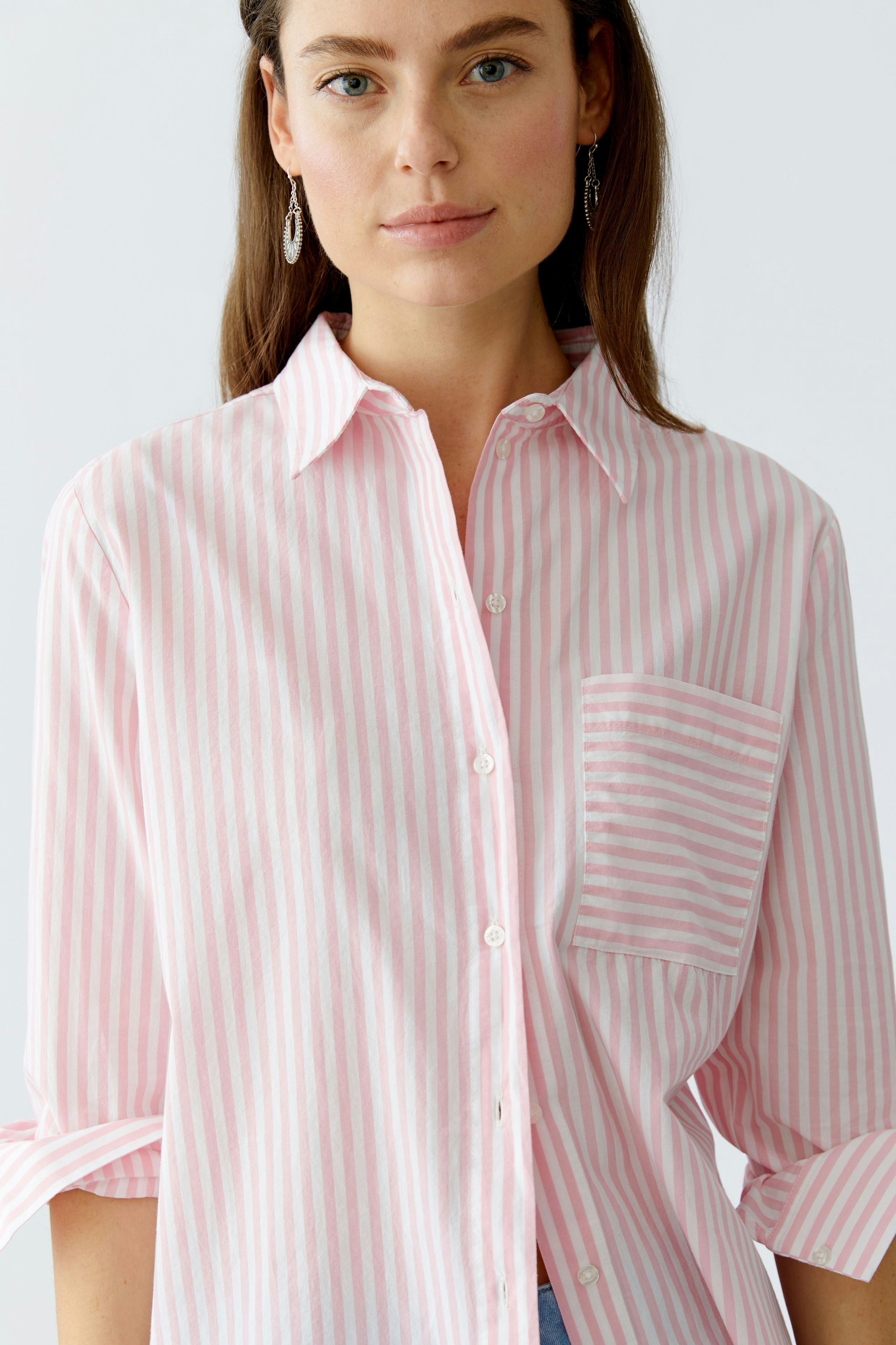 Hemdbluse: Frau trägt eine rosa-weiß gestreifte Bluse mit Brusttasche und lässigem Kragen.