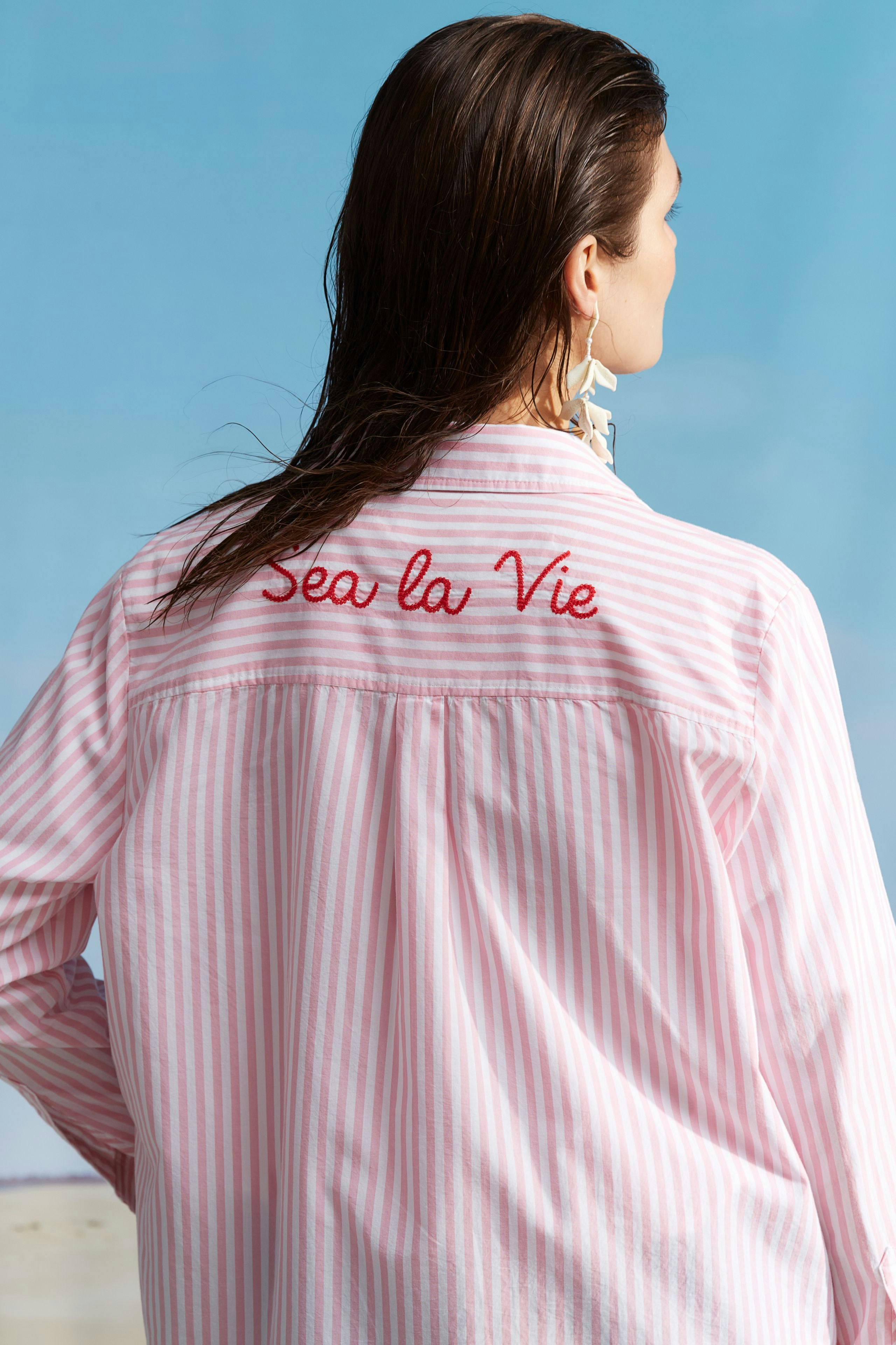 Hemdbluse: Frau trägt eine gestreifte Bluse mit dem Schriftzug 'Sea la Vie' auf dem Rücken.