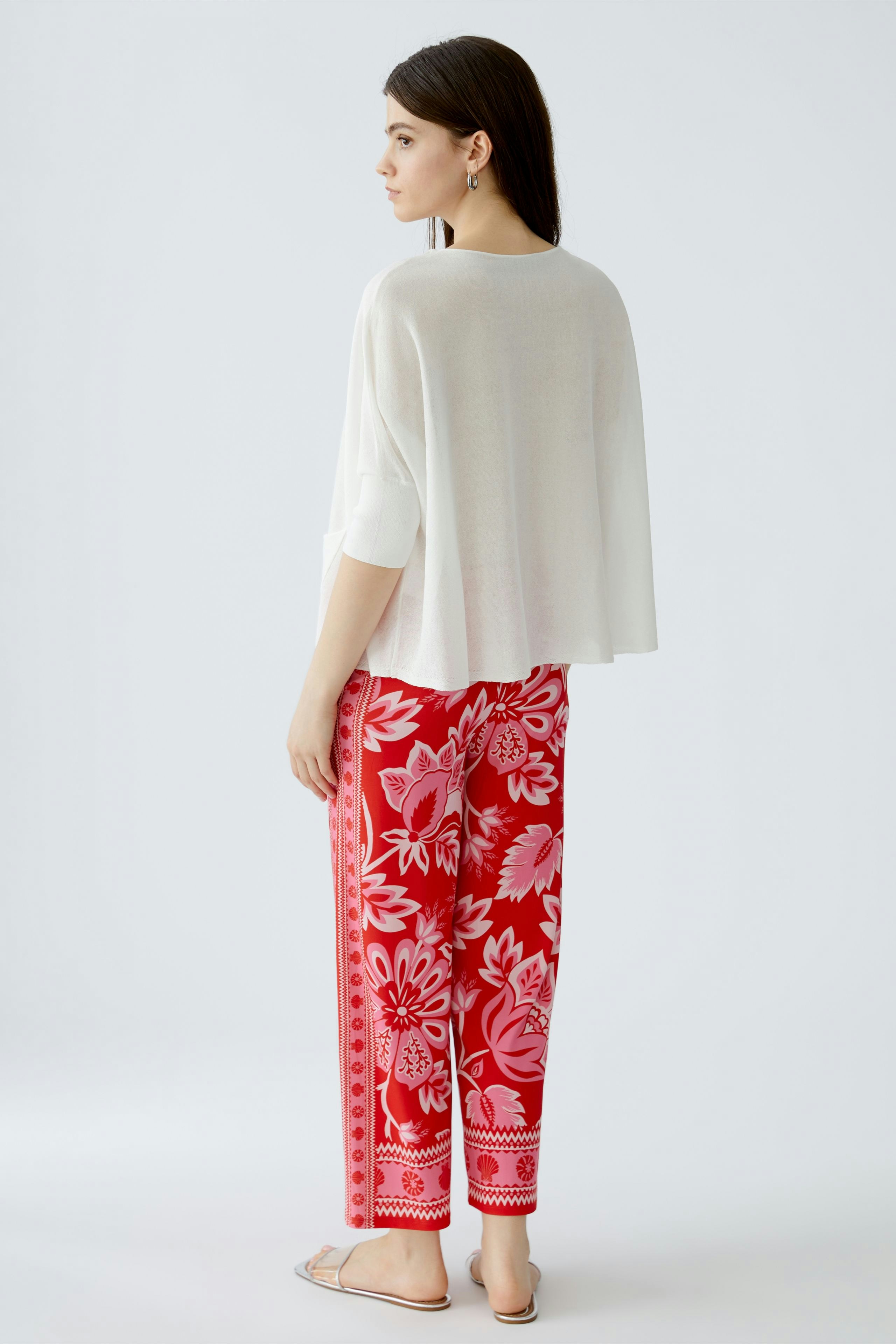 Damen-Pullover: Frau in weißem, lässigem Pullover mit weitem Schnitt und bunten, floralen Hosen.
