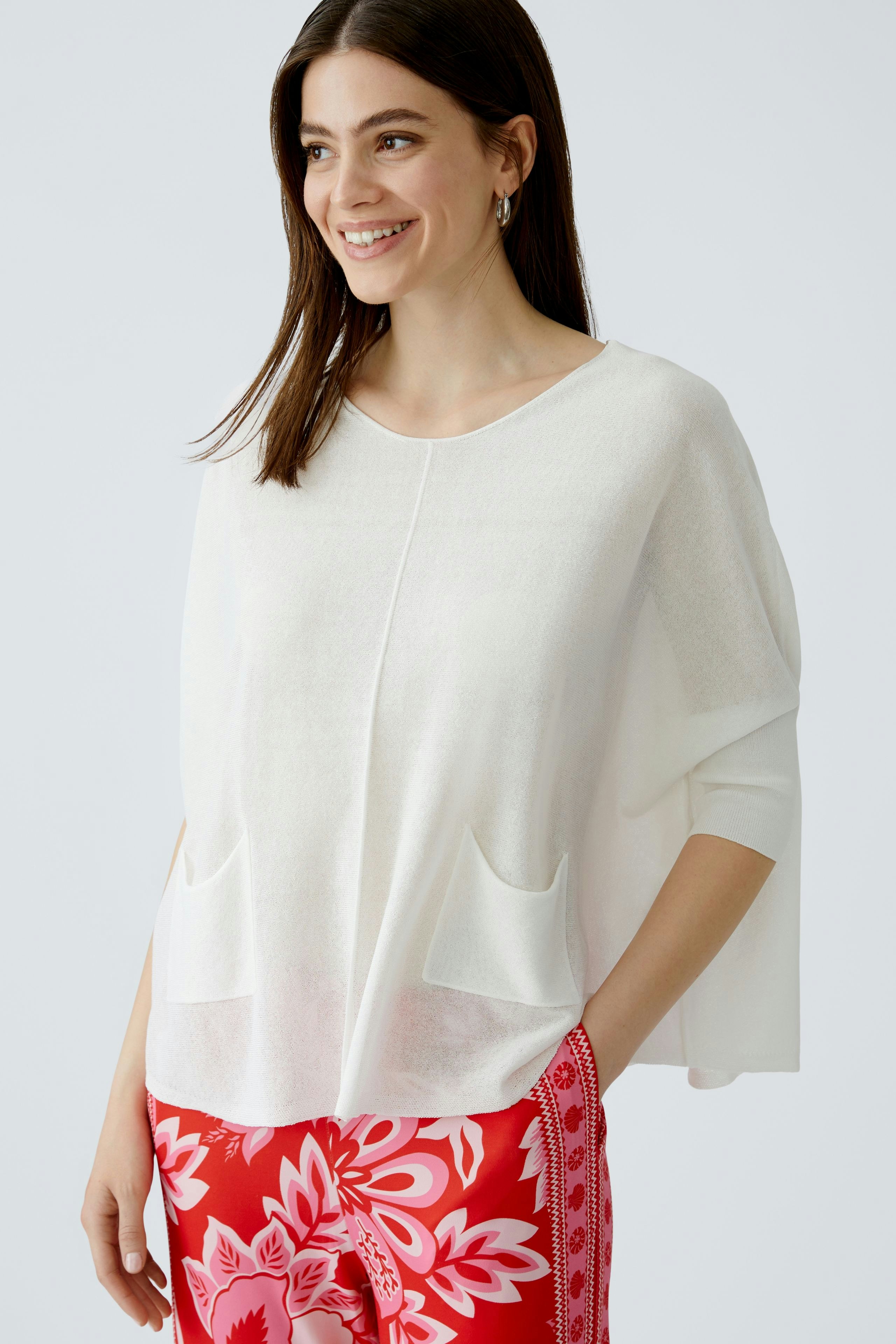 Damen-Pullover: Frau in weißem, lässigem Pullover mit Taschen und weitem Schnitt, kombiniert mit bunten Hosen.