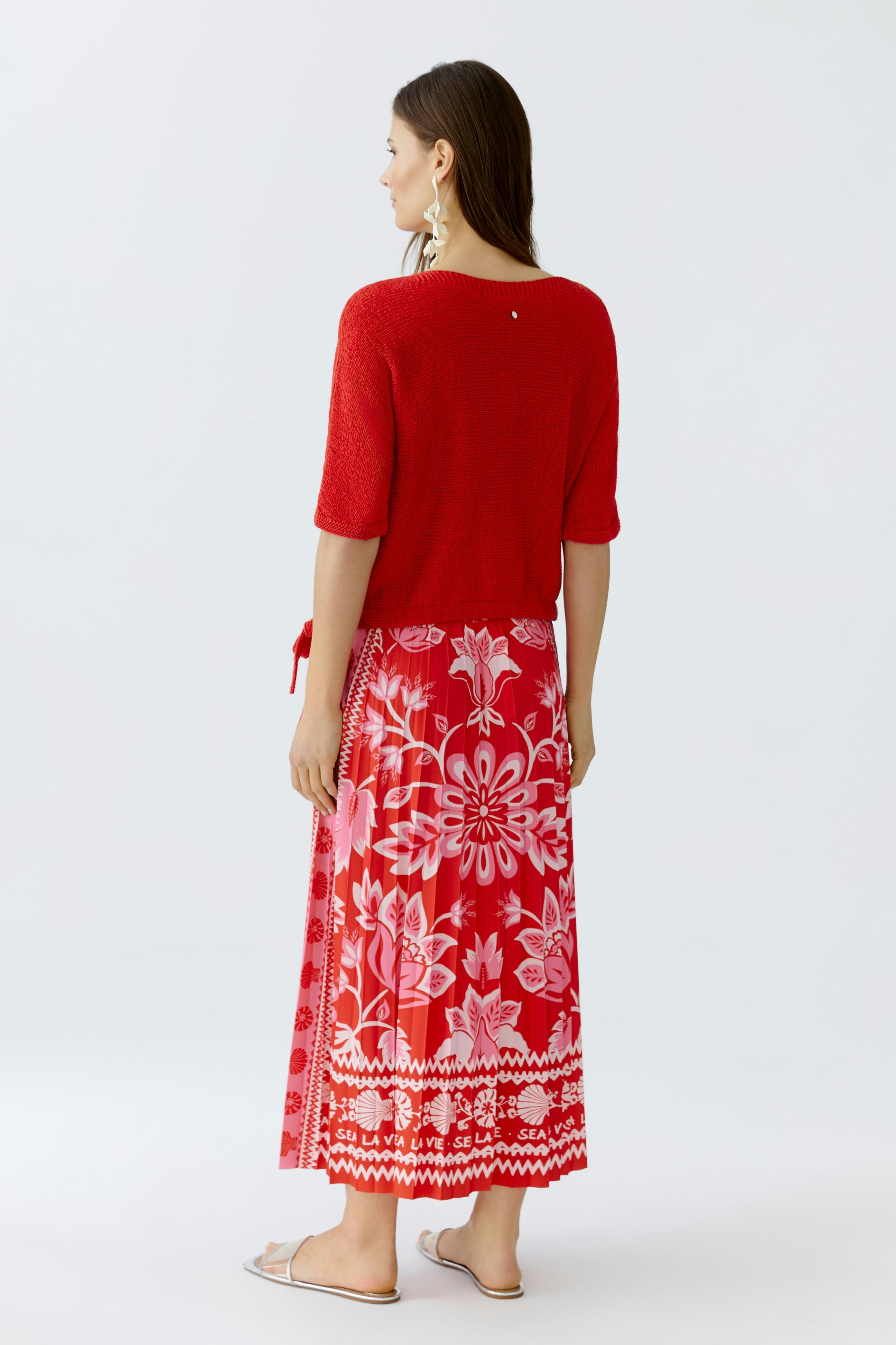 Casual women's pullover: A woman in a red knitted pullover with a relaxed fit and floral skirt.