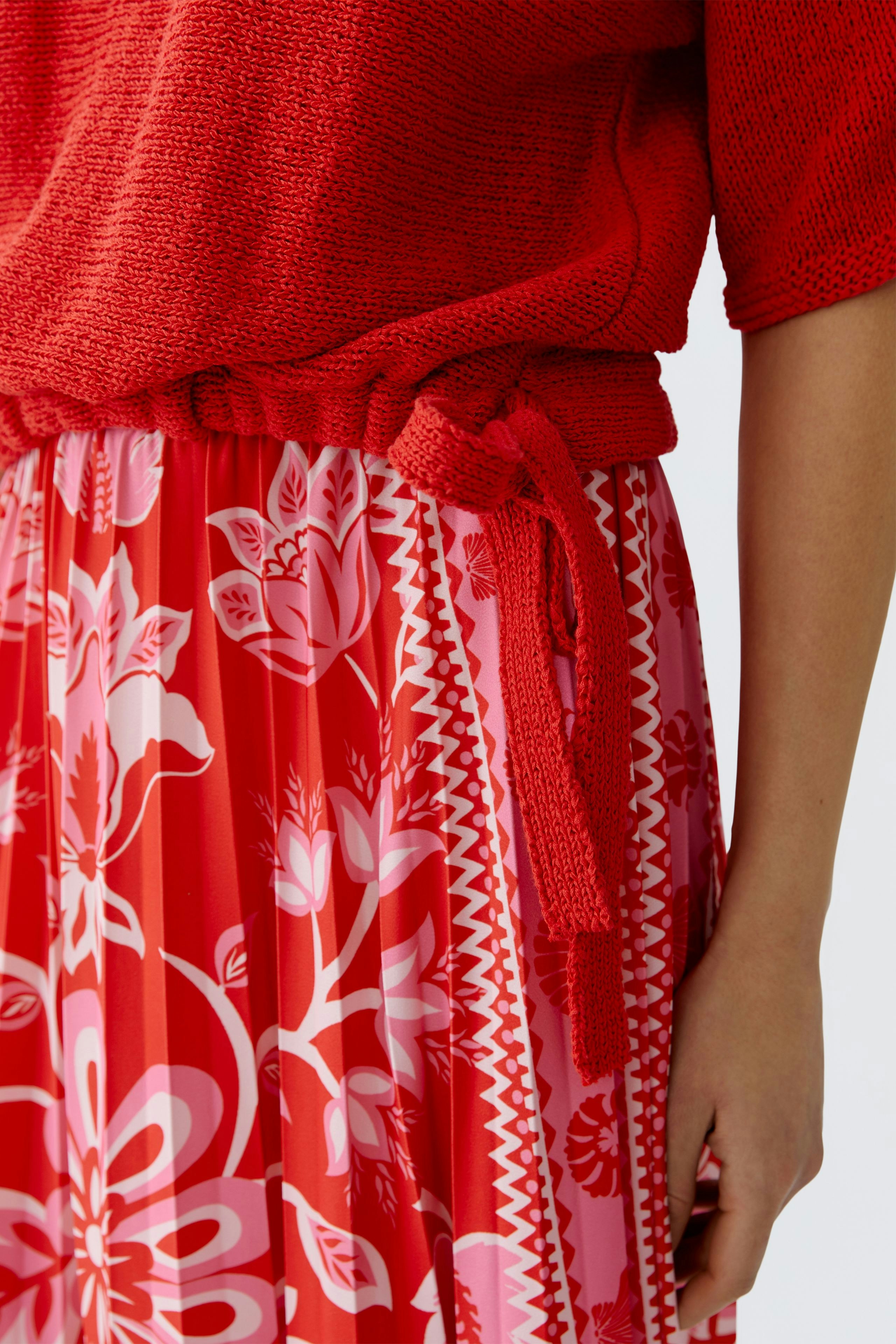 Casual women's pullover: A woman in a vibrant red knit pullover paired with a floral skirt.