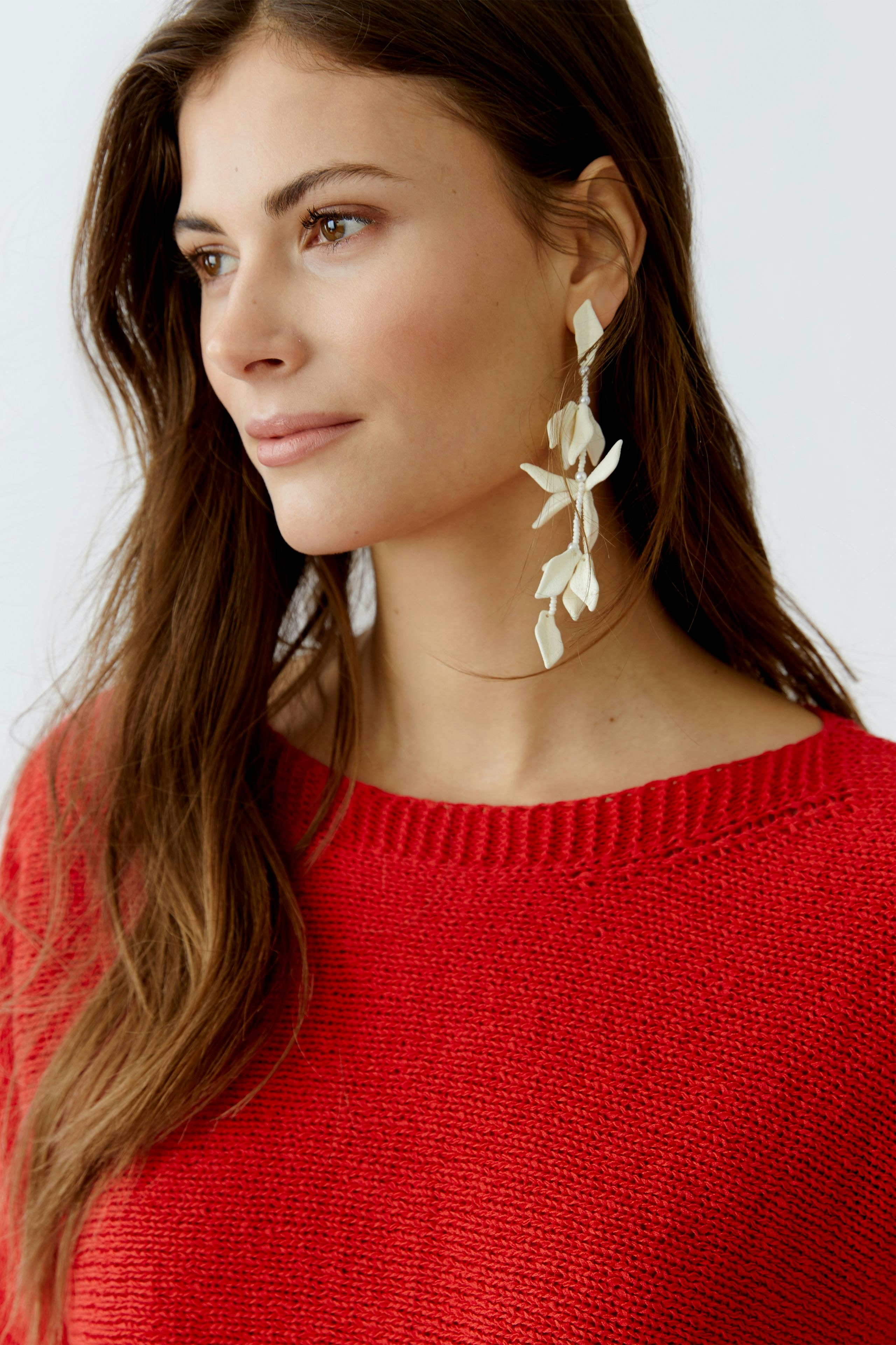 Modern women's pullover: A woman in a red knit pullover with a relaxed fit and stylish earrings.