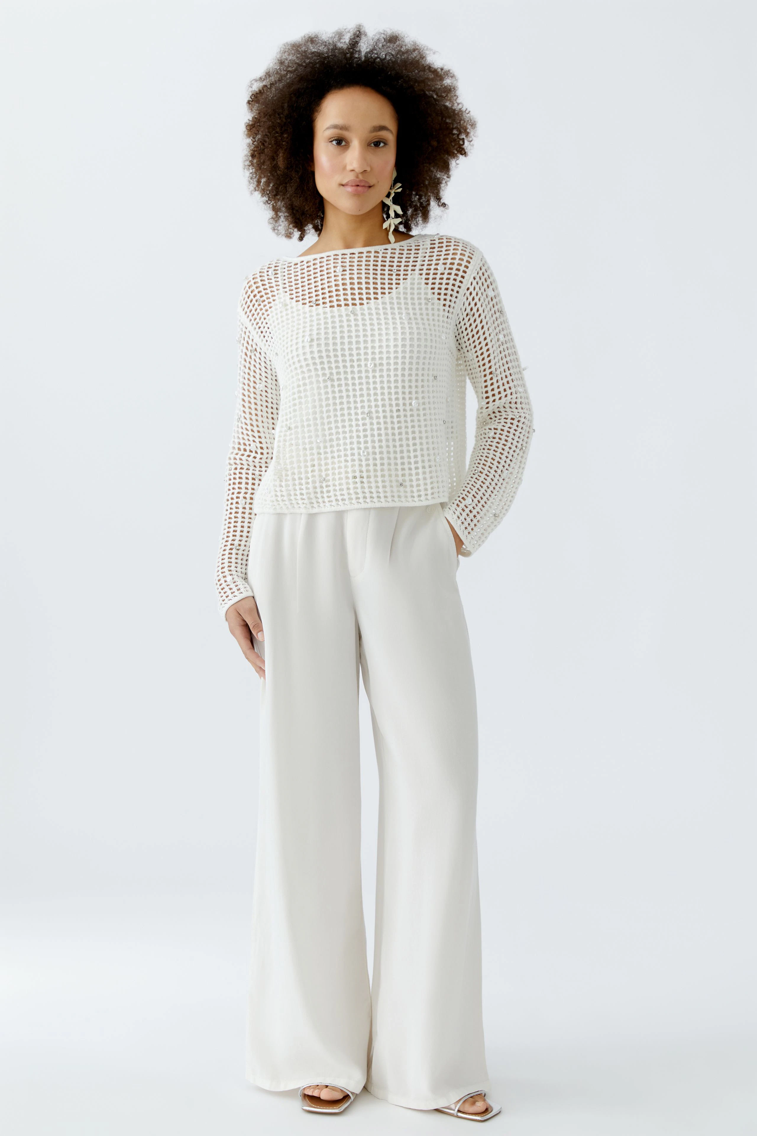Casual women's pullover: A woman in a white mesh pullover paired with light trousers stands confidently.